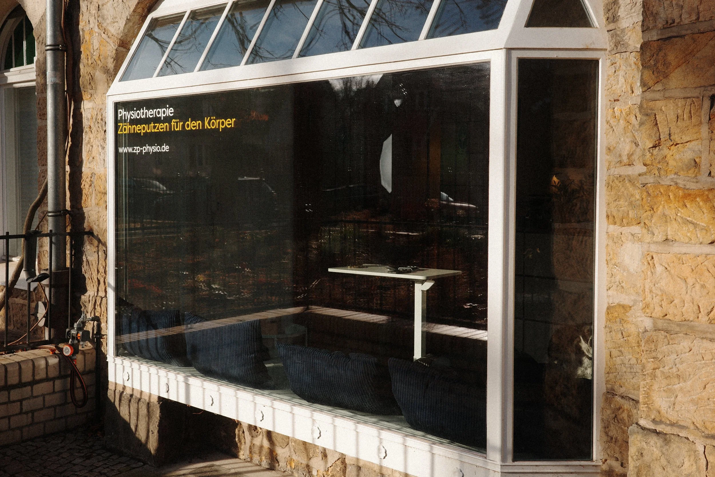 Außenansicht der Physiotherapiepraxis im Erdgeschoss eines Altbaus in Zehlendorf. Die Sonne scheint auf das Schaufenster.