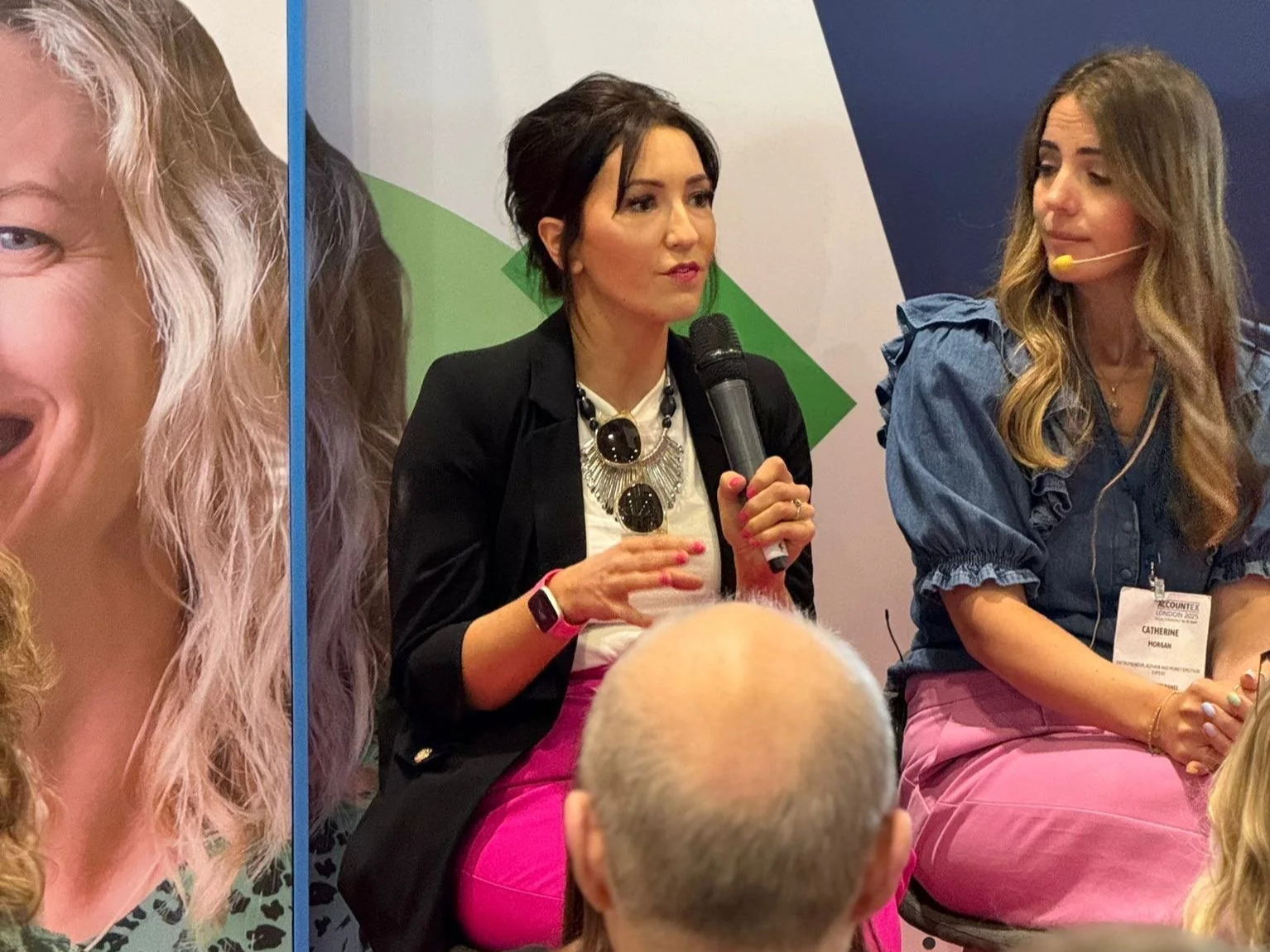 Woman speaking into a microphone at a panel discussion, with another woman sitting next to her, both wearing conference badges, against a colorful conference backdrop.