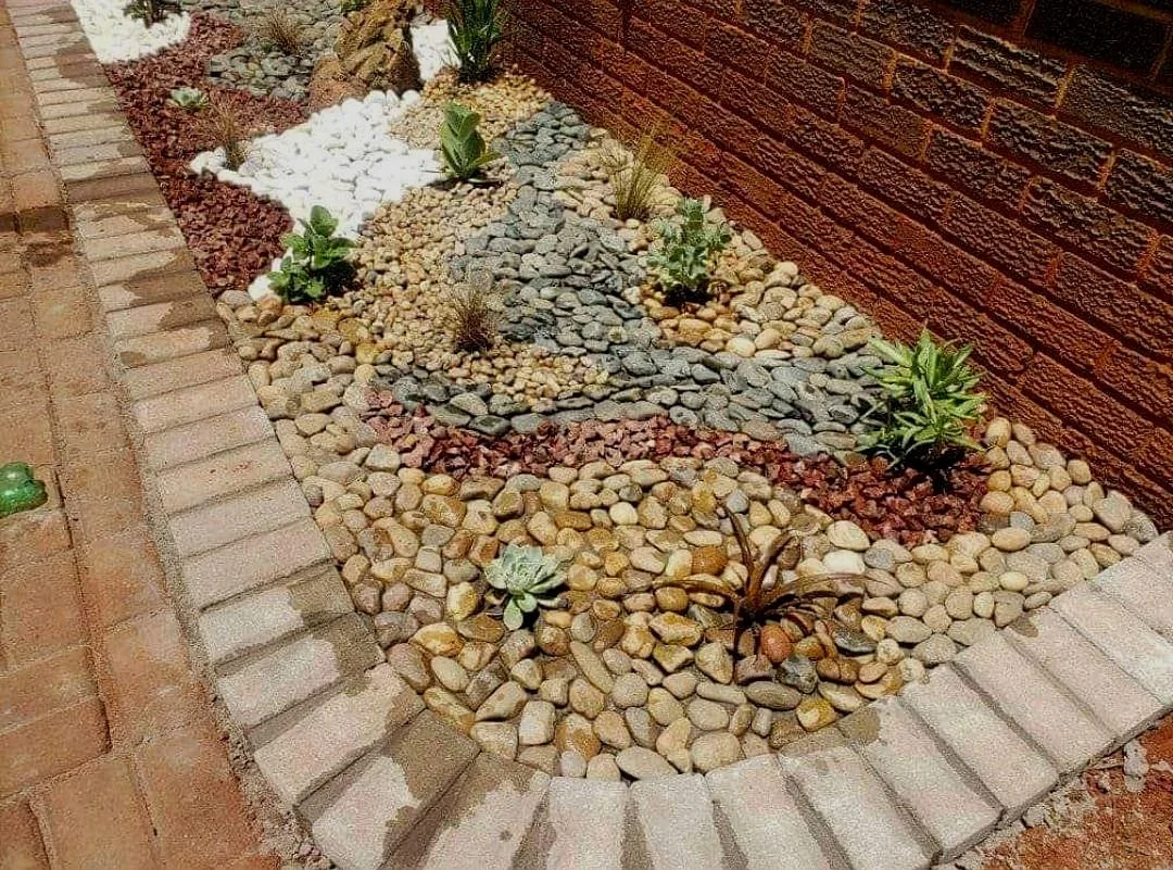 A garden bed with white, black and mixed pebbles in amongst red crush.