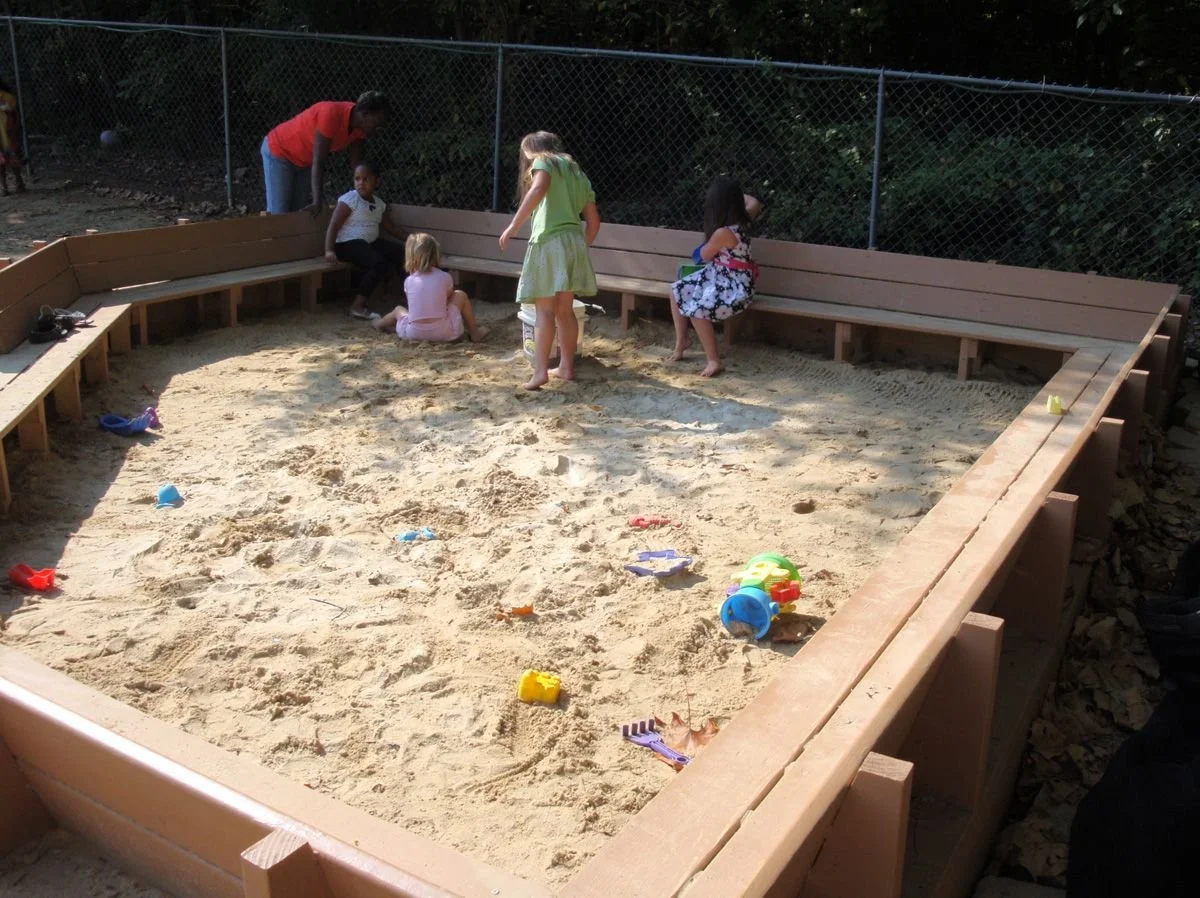 Children playing in playpit sand with toys.