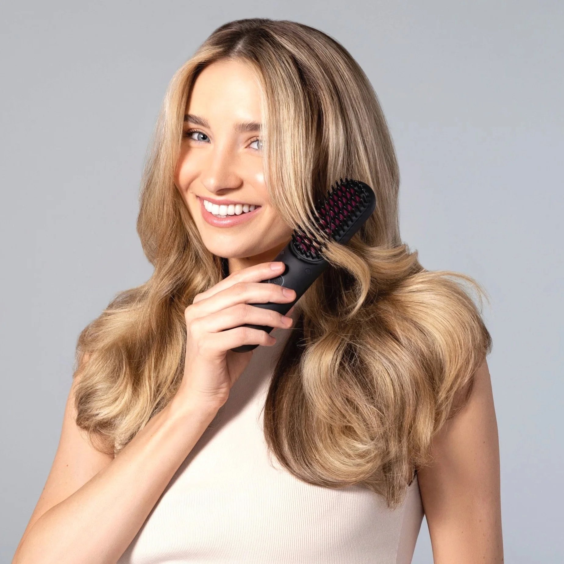 Una mujer sonriendo mientras se peina el cabello con un cepillo eléctrico