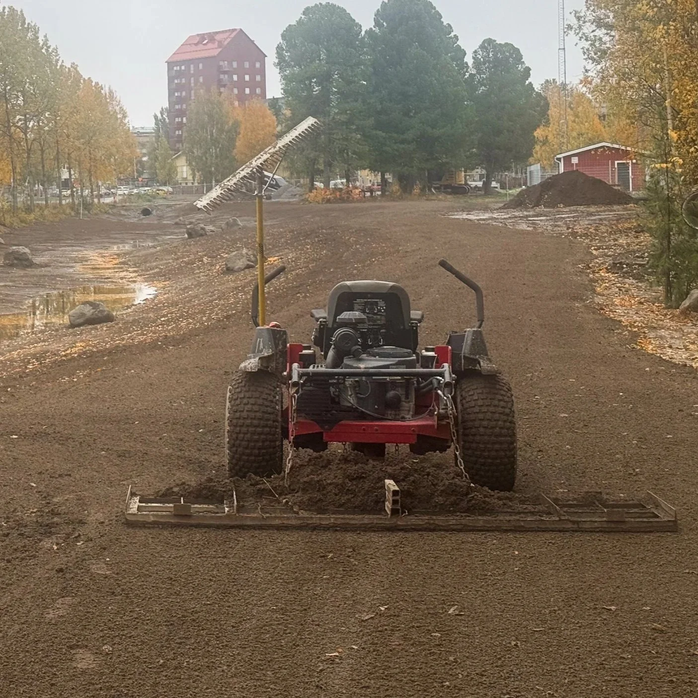 En liten grävmaskin vid en sjö på en grönd äng under en blå himmel.