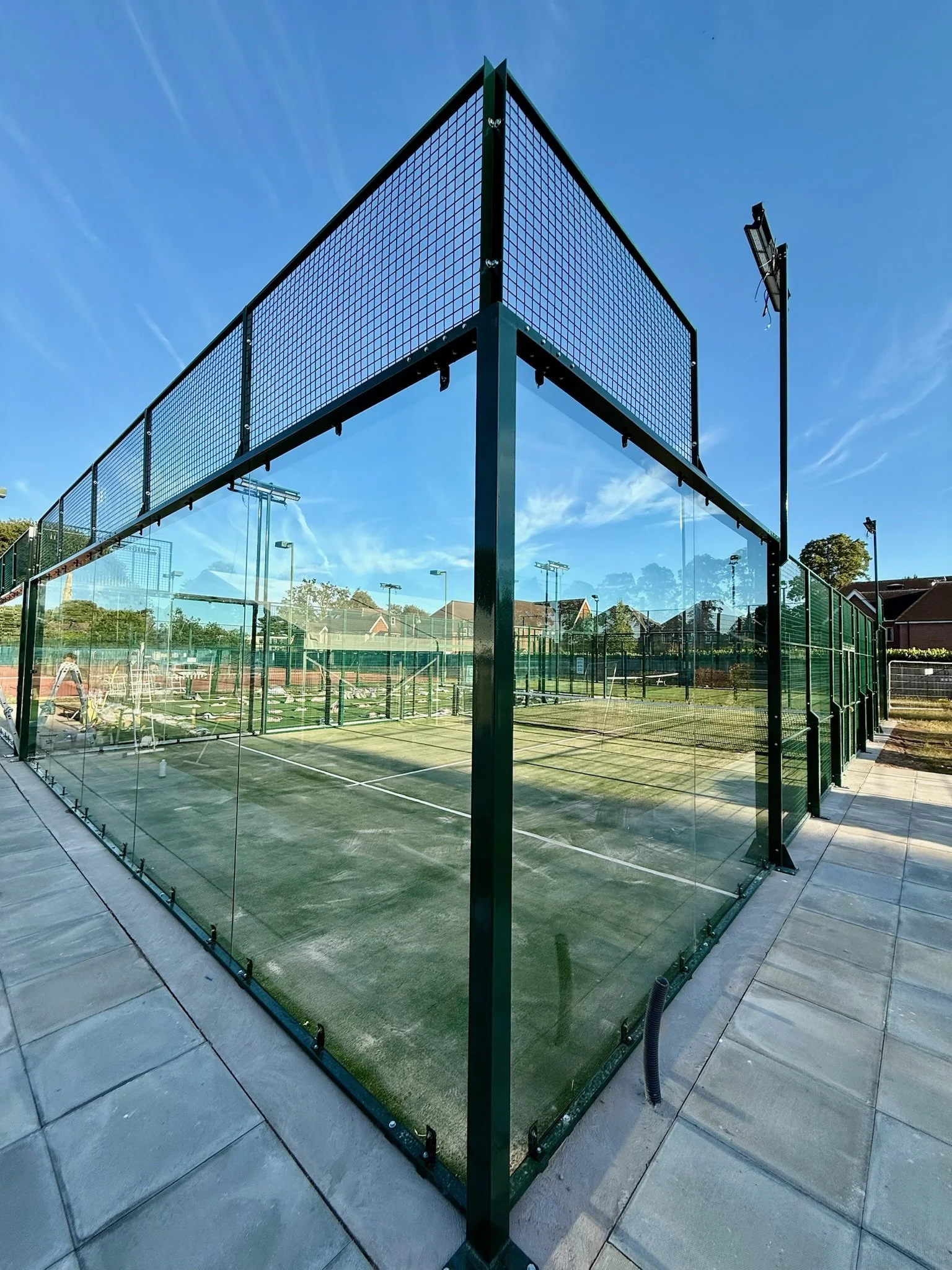 Outdoor padel or pickleball courts with enclosed glass walls and a net against a clear blue sky.
