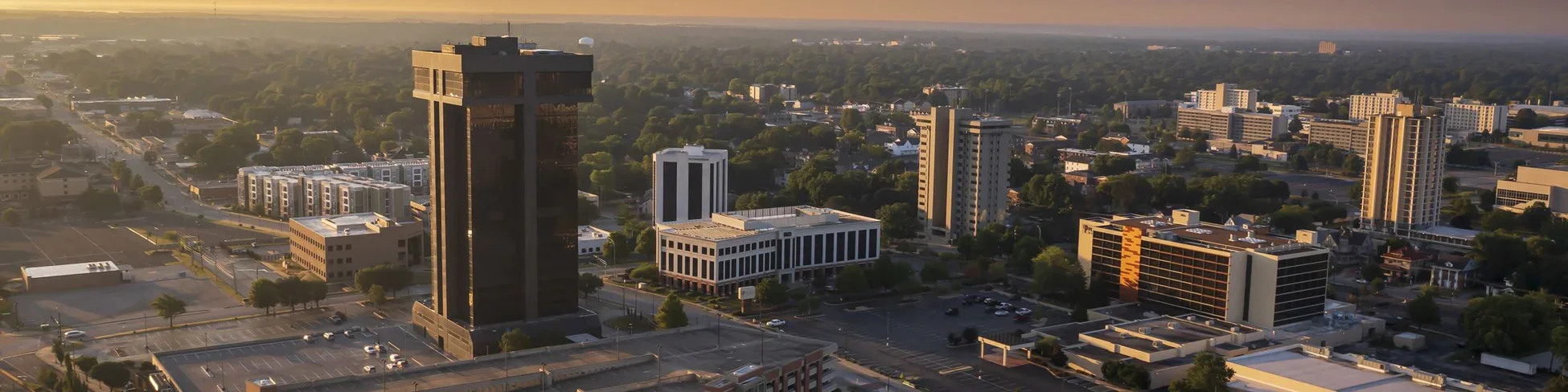 Aerial view of Springfield Missouri cityscape at sunset with tall buildings, parking lots, and trees.