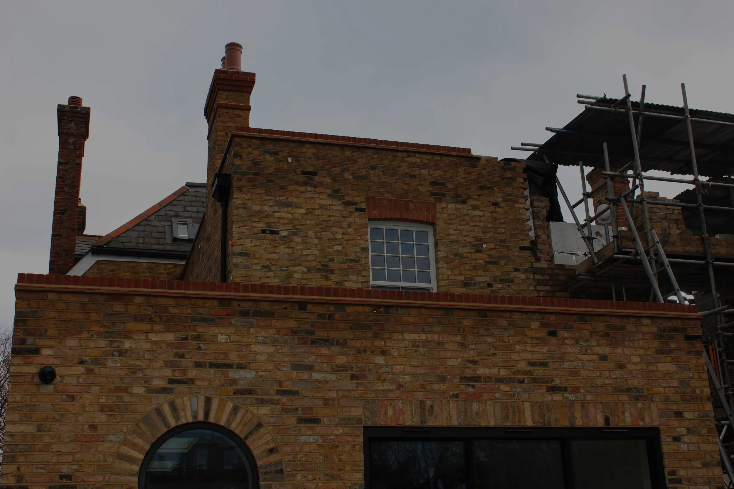 A brick building under renovation with scaffolding on the right side and a cloudy sky above.