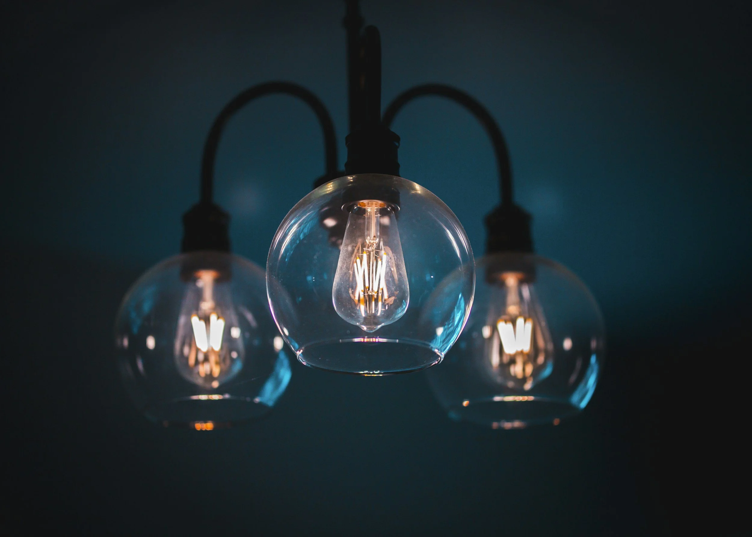 Three modern hanging light fixtures with clear glass globe covers and filament bulbs against a dark background.
