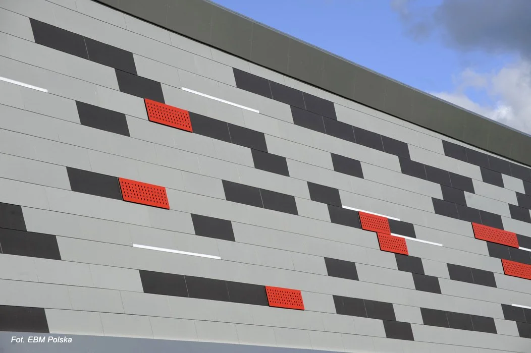 Close-up of a modern building facade with a pattern of black, gray, and white rectangular tiles and red perforated panels.