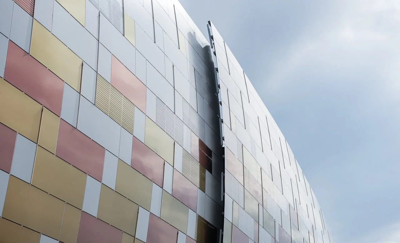 Modern building facade with colorful square panels and vertical black strips, under a cloudy sky.