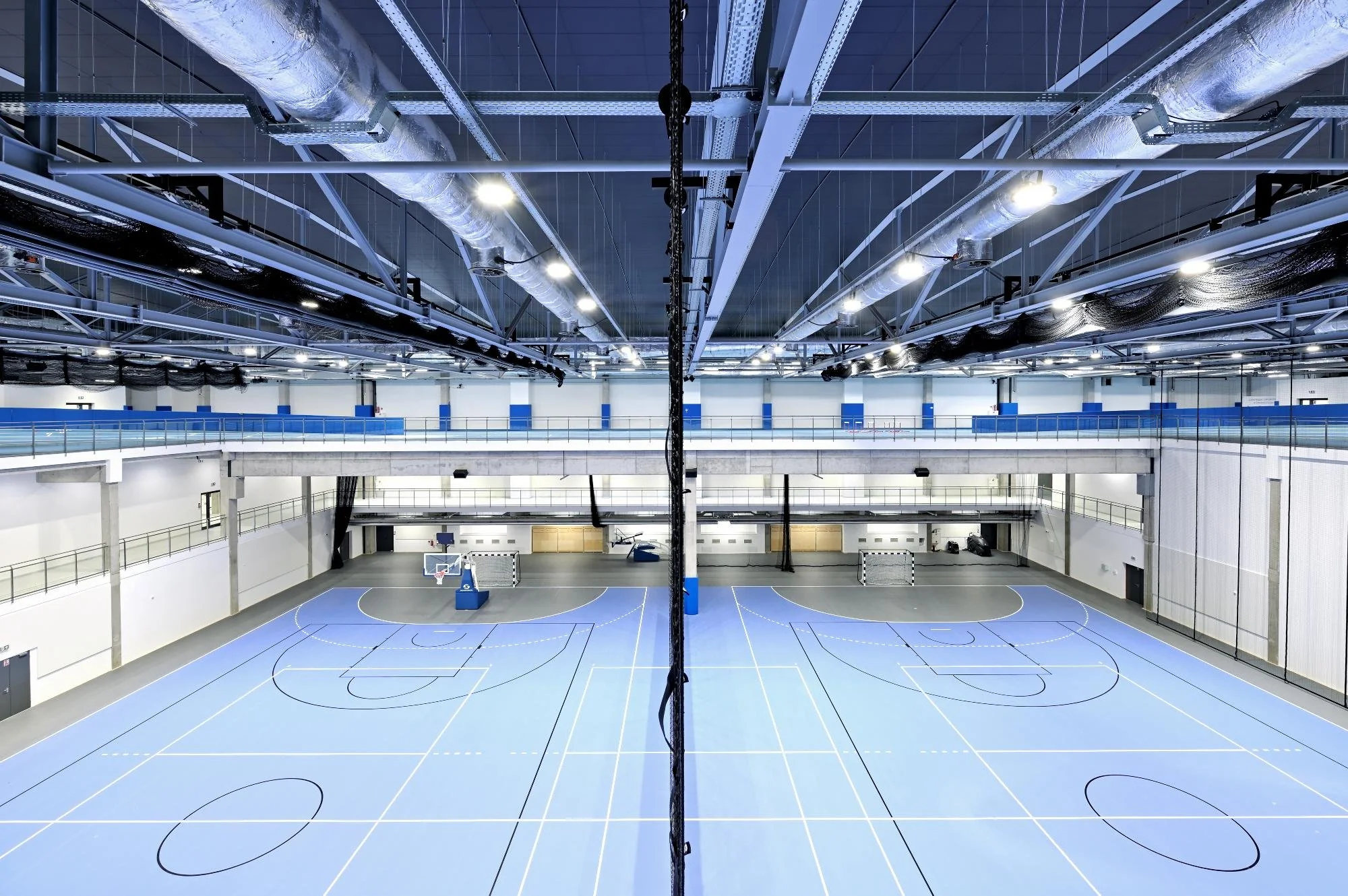 Empty indoor sports arena with basketball courts and blue flooring, viewed from above.