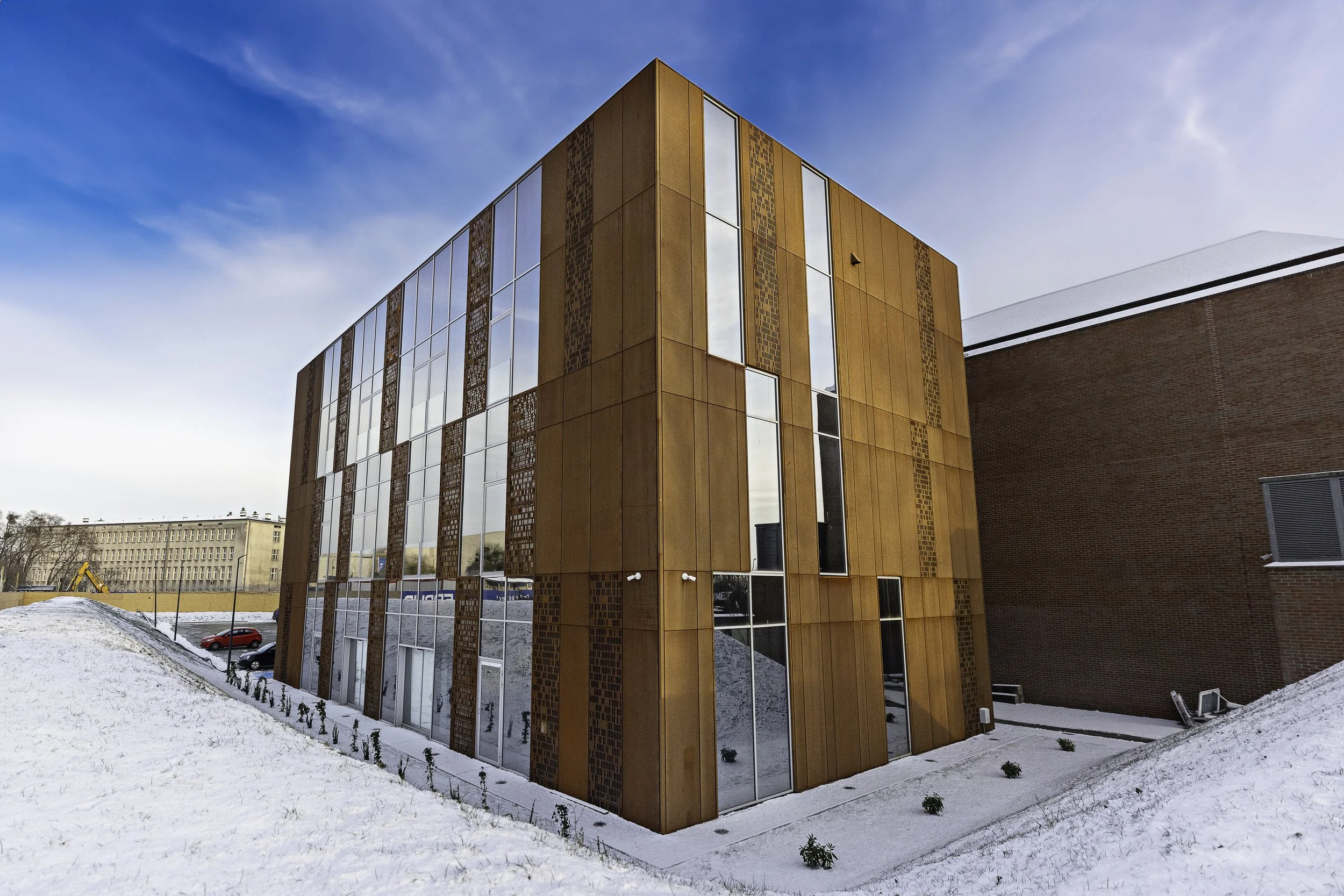A modern building with a rust-colored facade and large glass windows, surrounded by snow on the ground.