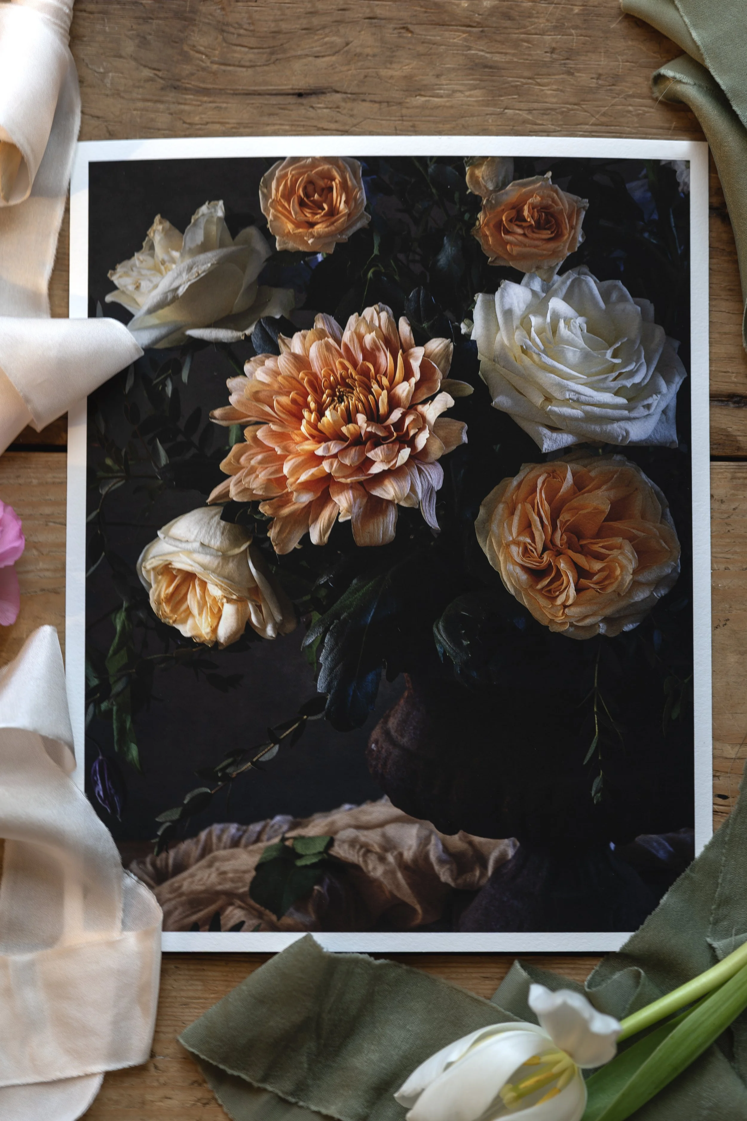 A photograph of a floral print lying on a wooden surface, surrounded by various fabric swatches and flowers.