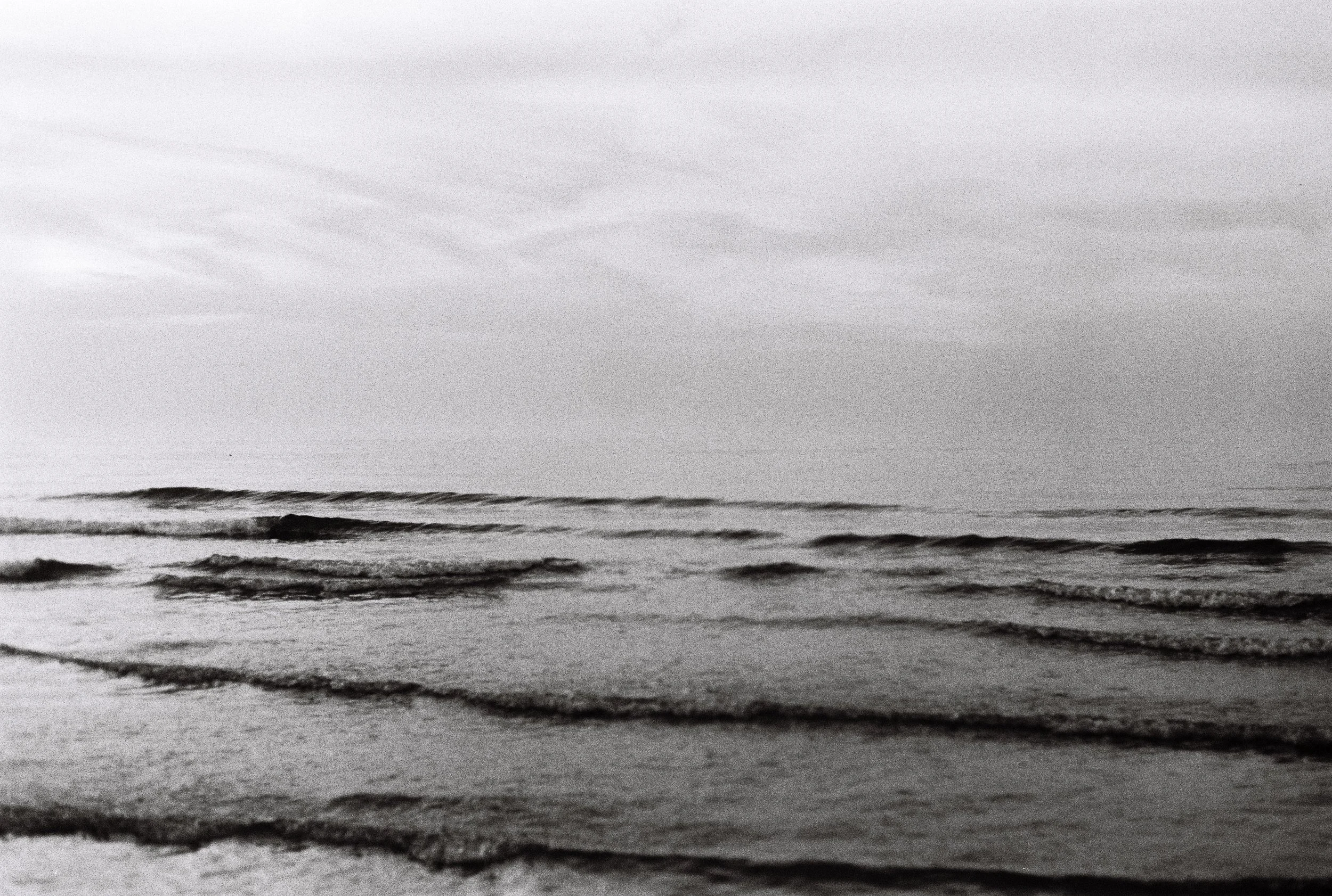 Plage calme avec vagues douces sous un ciel nuageux en noir et blanc.