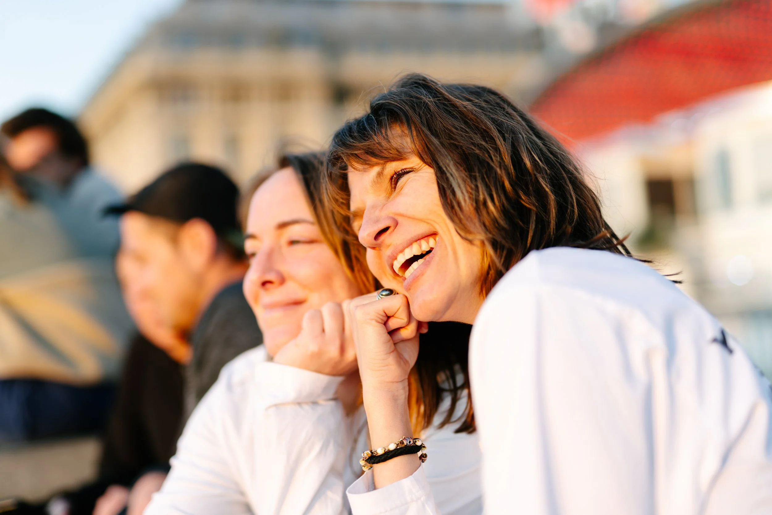 Groupes de personnes souriantes assises dans un environnement urbain, probablement lors d'une journée ensoleillée.