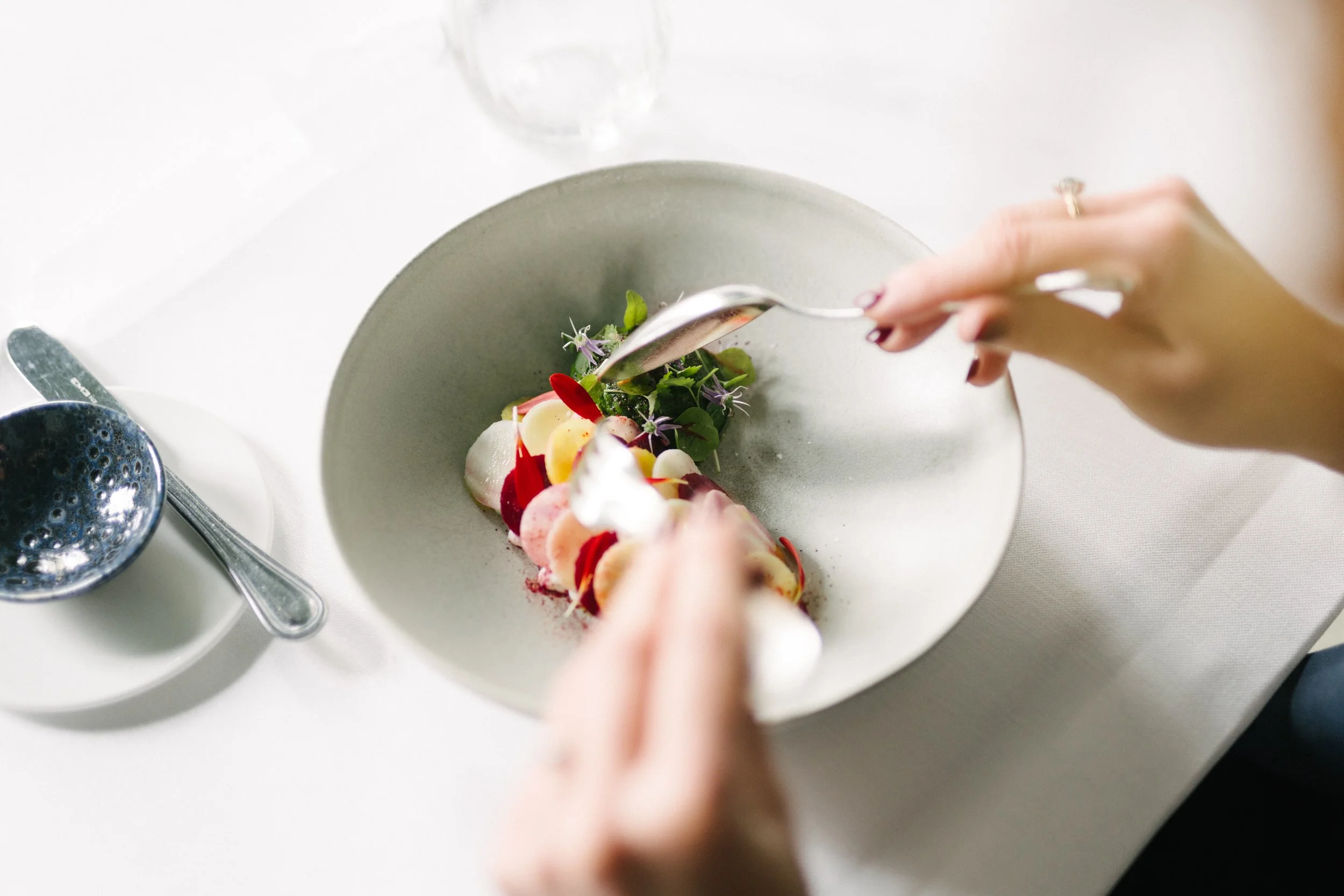 Une personne en train de déguster un plat gastronomique sophistiqué dans une assiette blanche.