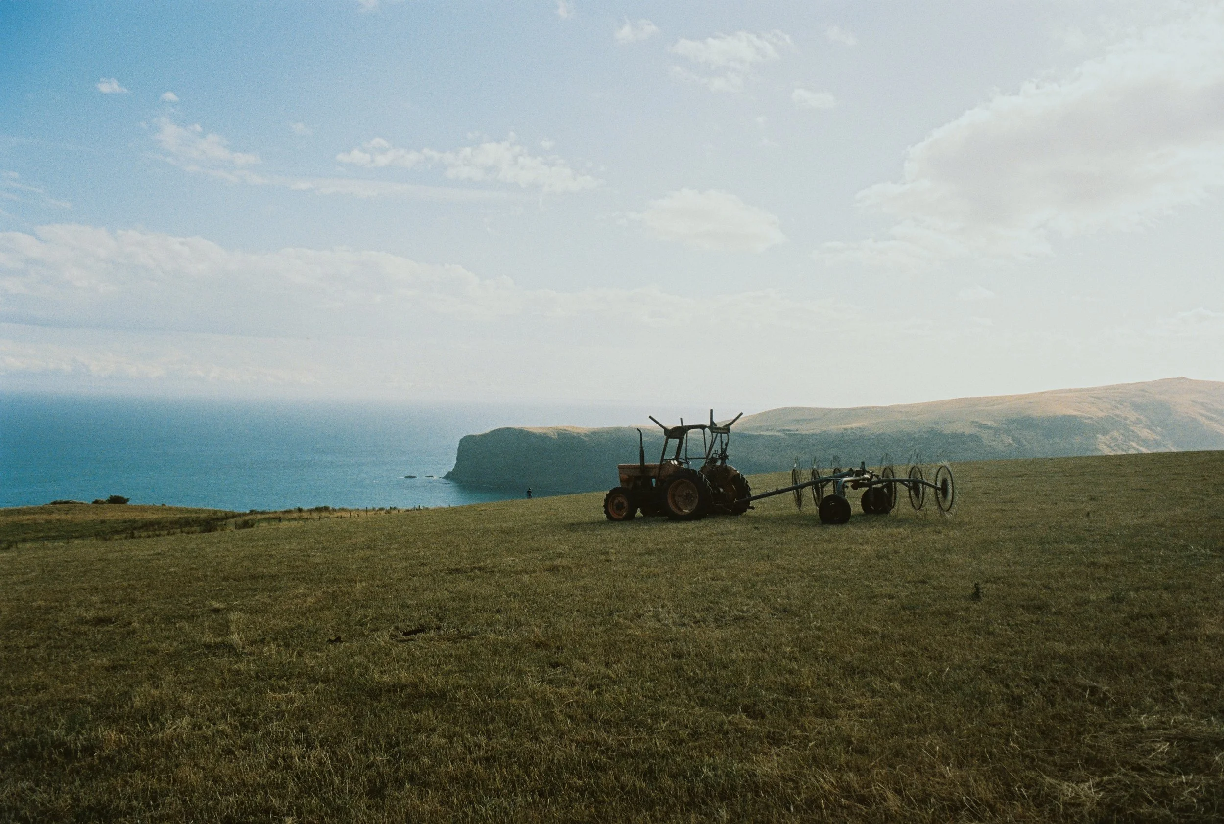 Un tracteur abandonné sur un champ avec la mer en arrière-plan et un ciel bleu avec quelques nuages.