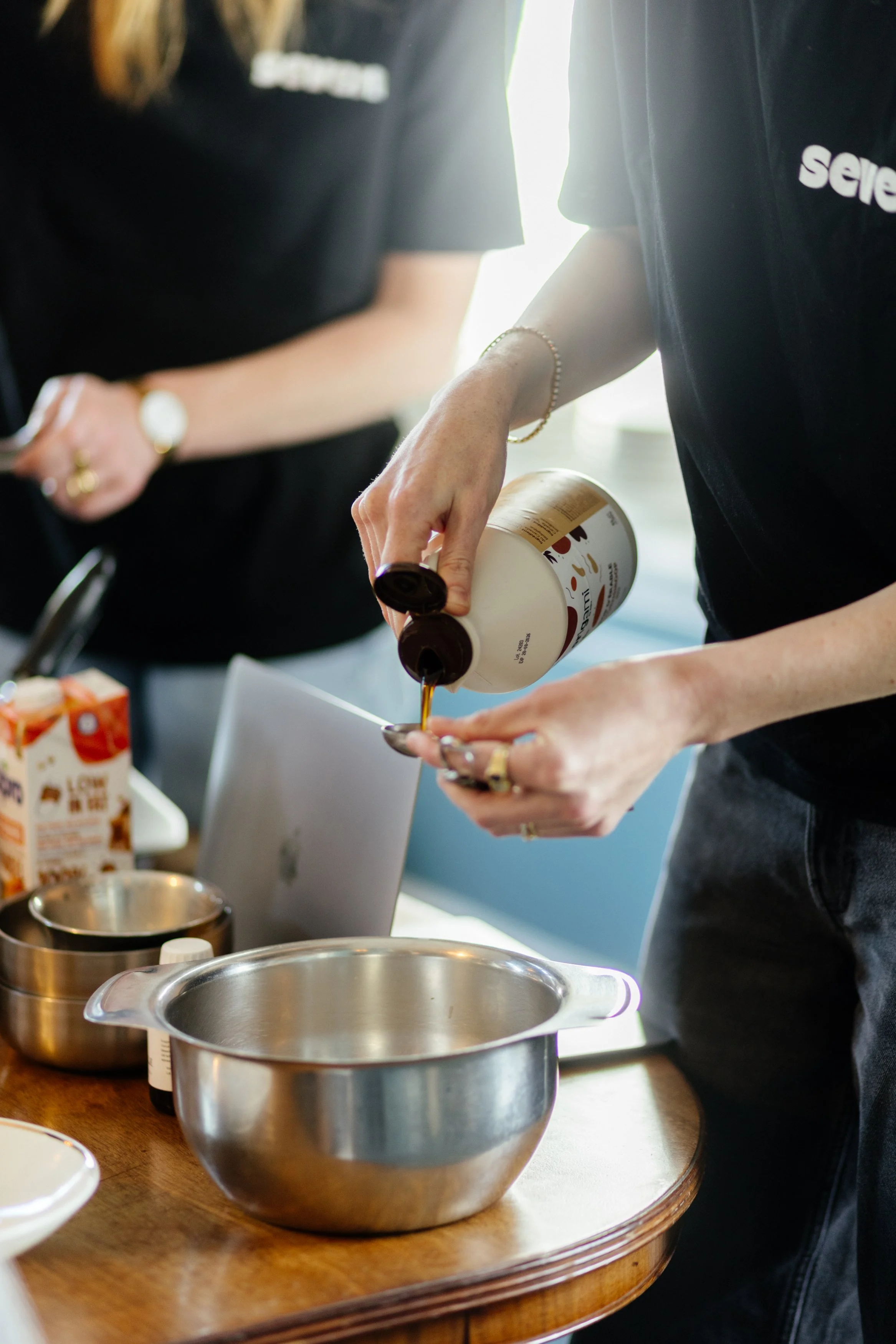 Une personne verse du sirop dans une cuillère lors d'une démonstration culinaire, devant un table avec divers ustensiles et emballages de nourriture.