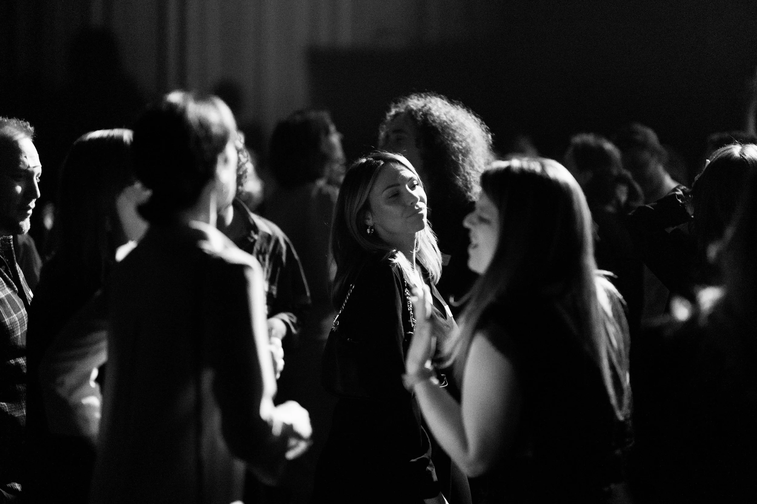 Groupe de personnes dansant au bal, illuminé par des lumières basses, ambiance festive en noir et blanc.