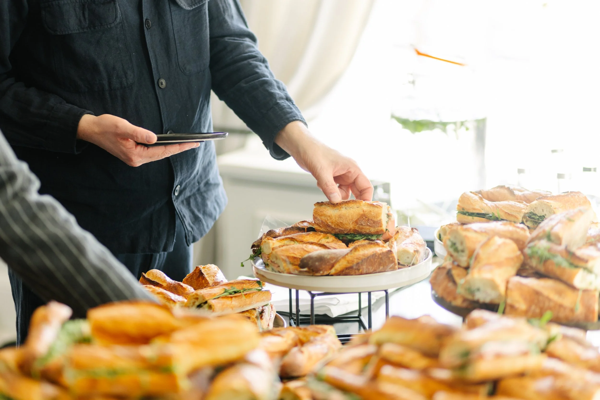 Personne choisissant un sandwich dans une sélection de sandwichs variés sur une table lumineuse.