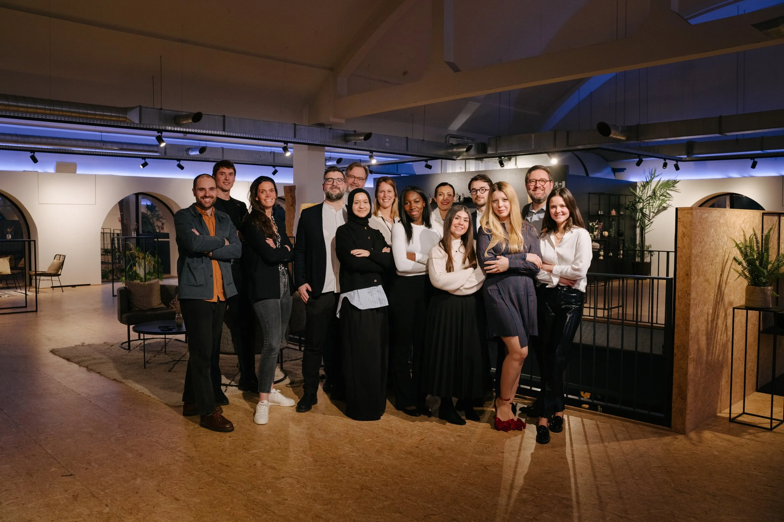 Groupe de 13 personnes posant ensemble dans un espace intérieur moderne avec décoration végétale, lumière tamisée et mobilier contemporain.