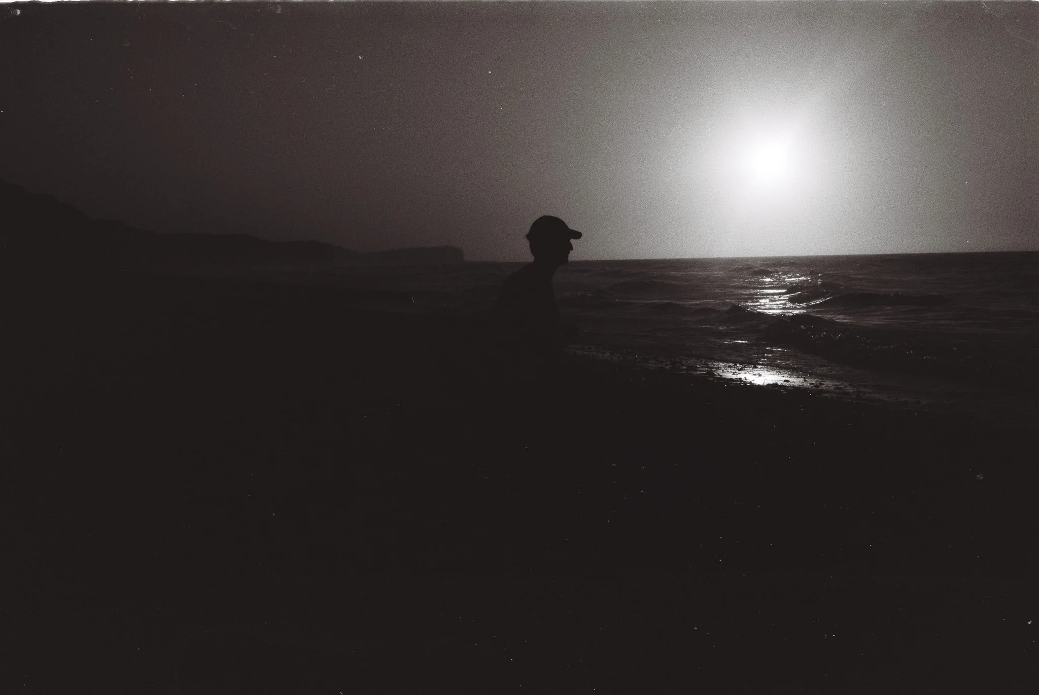 Silhouette d'une personne assise sur la plage sous la lumière de la lune, avec la mer en arrière-plan.