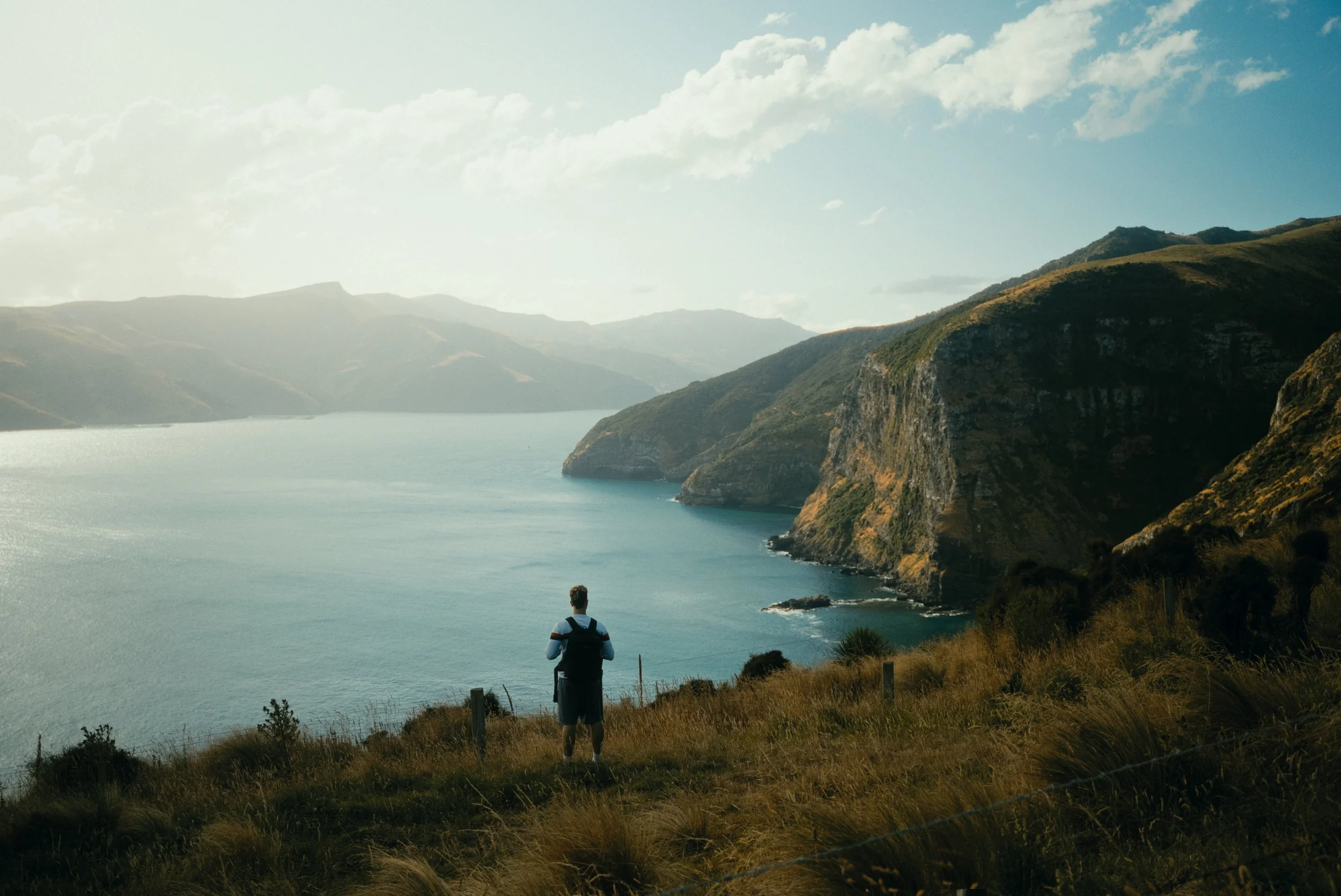 Une personne avec un sac à dos regarde un paysage de lac et de montagnes.