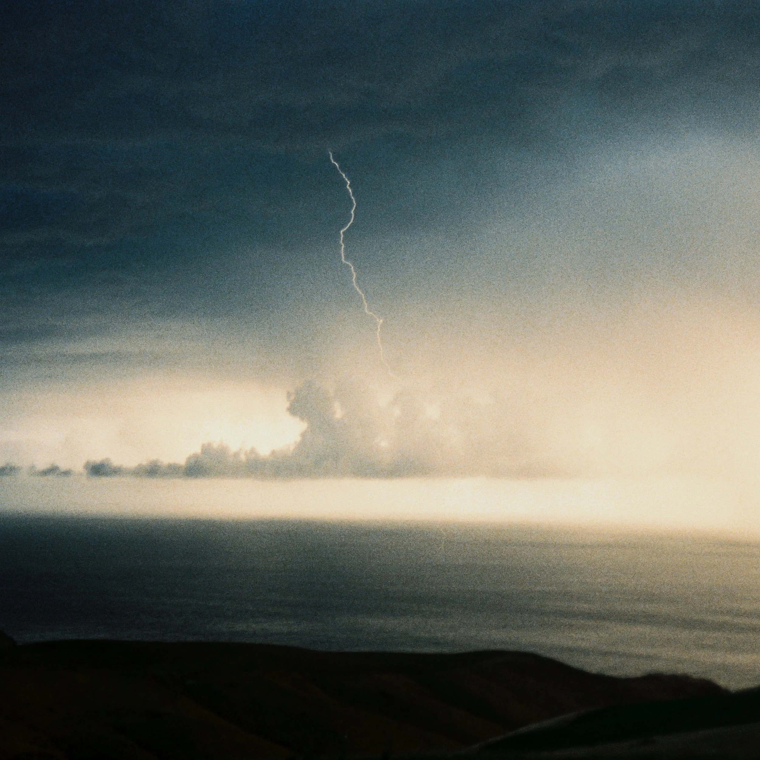 Foudre illuminant un ciel nuageux au-dessus de l'océan, vue d'une zone côtière, créant une ambiance dramatique.