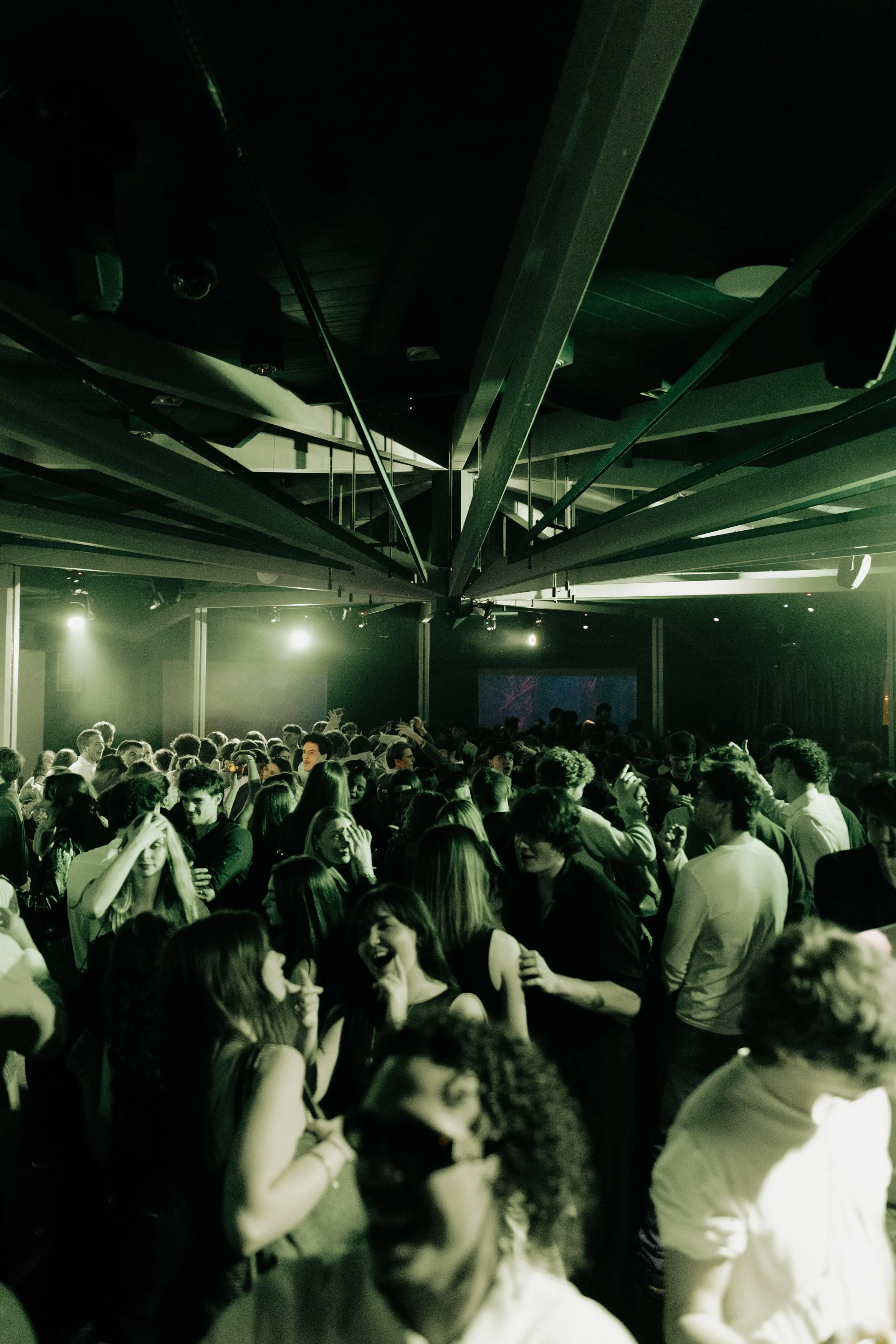Foule de jeunes dansant et socialisant lors d'une soirée dans un club avec éclairage vert.