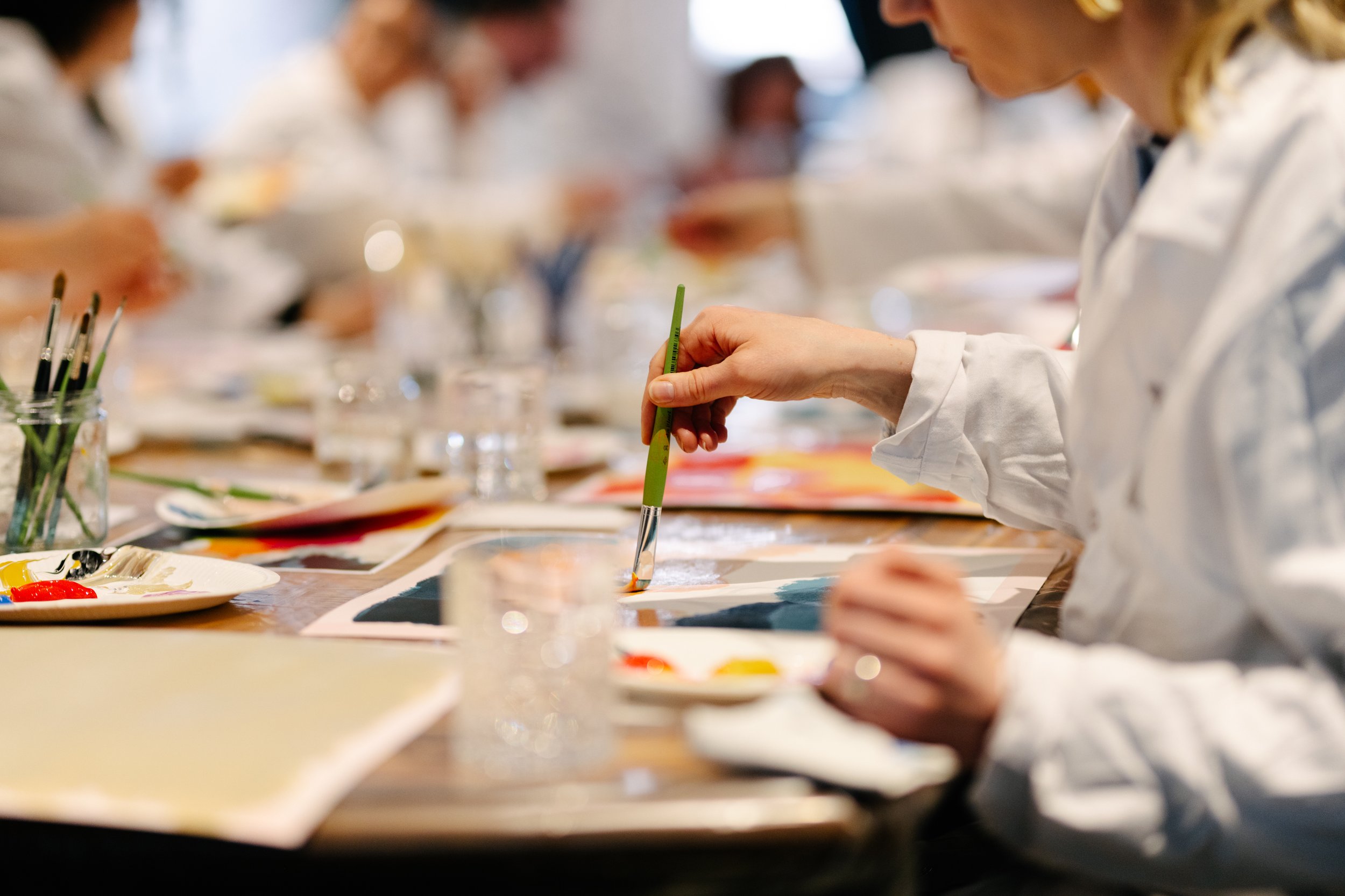 Groupe de personnes en blanc participant à un atelier de peinture, assis autour d'une table avec des matériaux de peinture.