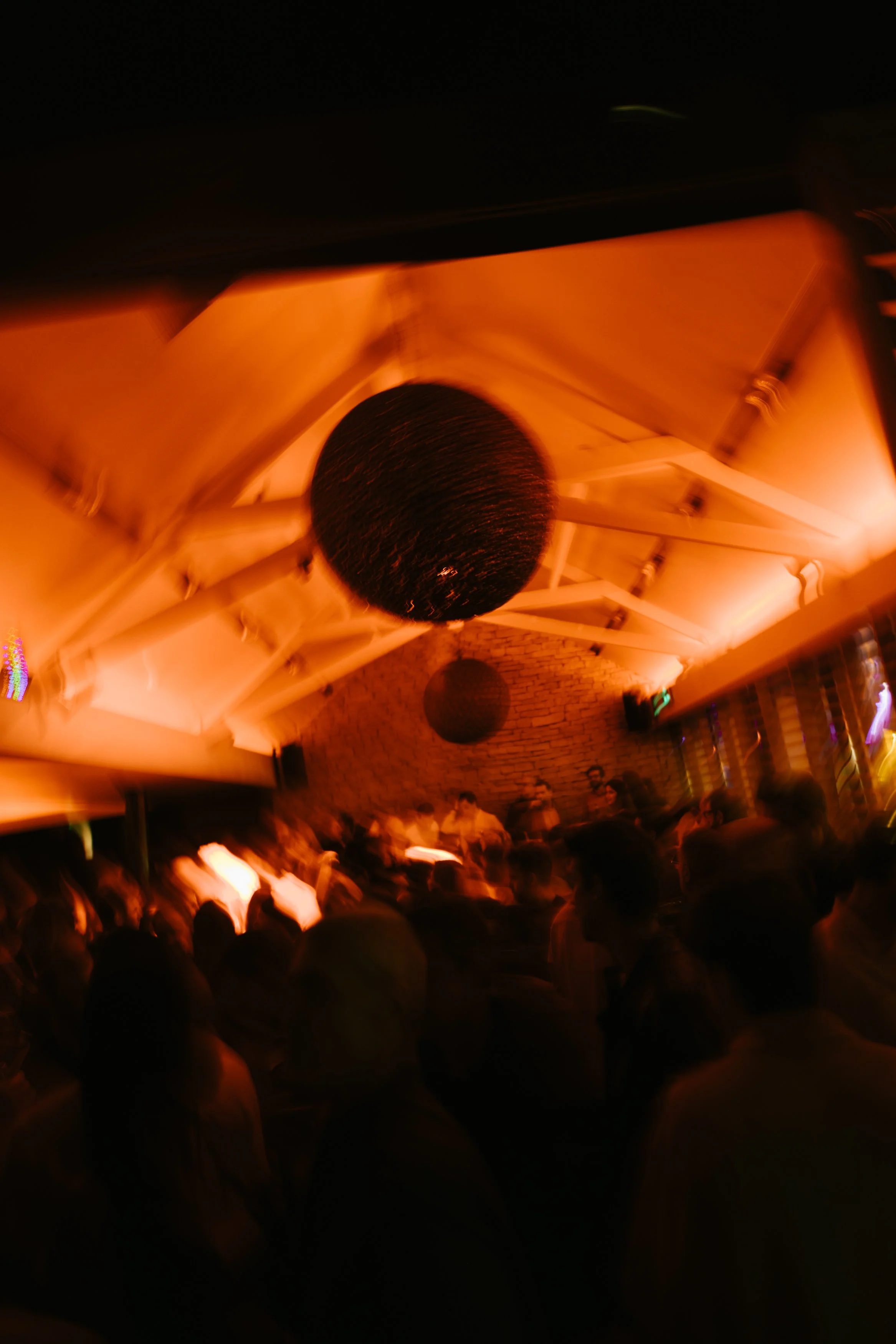 Une scène en club ou en discothèque avec des personnes dansant et un éclairage orange chaud et des ballons noirs suspendus au plafond.