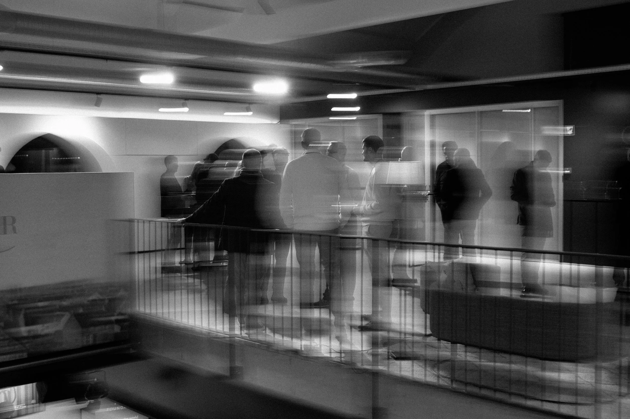 Groupe de personnes discutant dans un espace intérieur, photographie en noir et blanc avec un effet de mouvement.