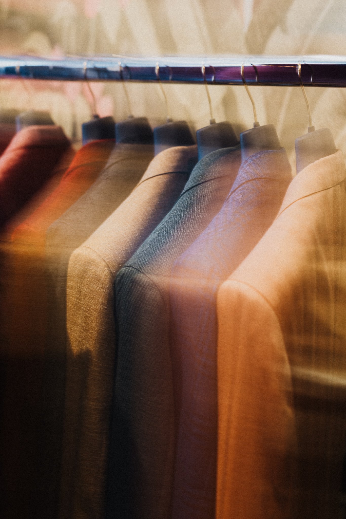 Une rangée de costumes colorés suspendus sur une tringle dans une boutique de vêtements.