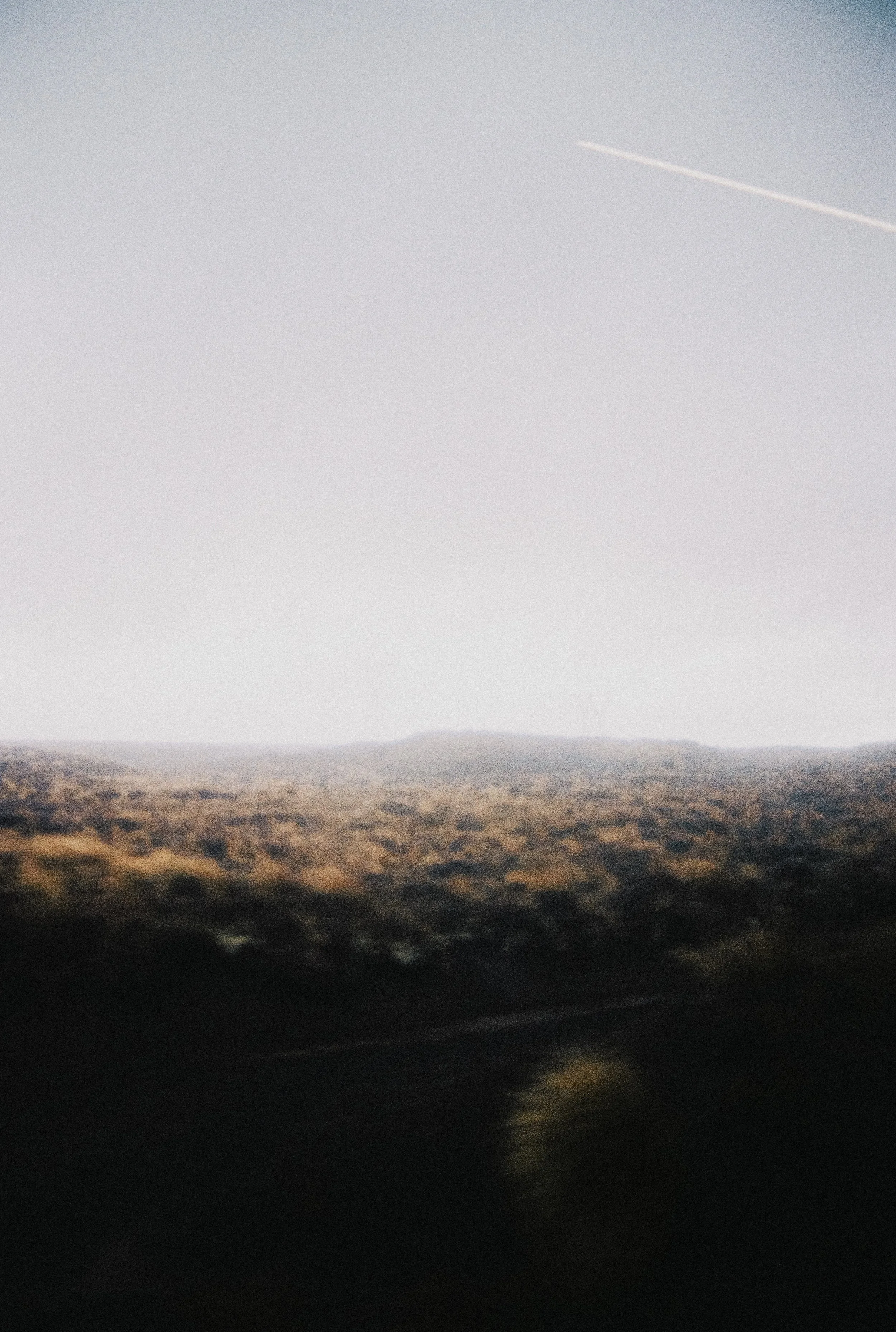 Paysage rural avec un ciel clair et une traînée d'avion, vue de la route avec des collines ou champs en arrière-plan.
