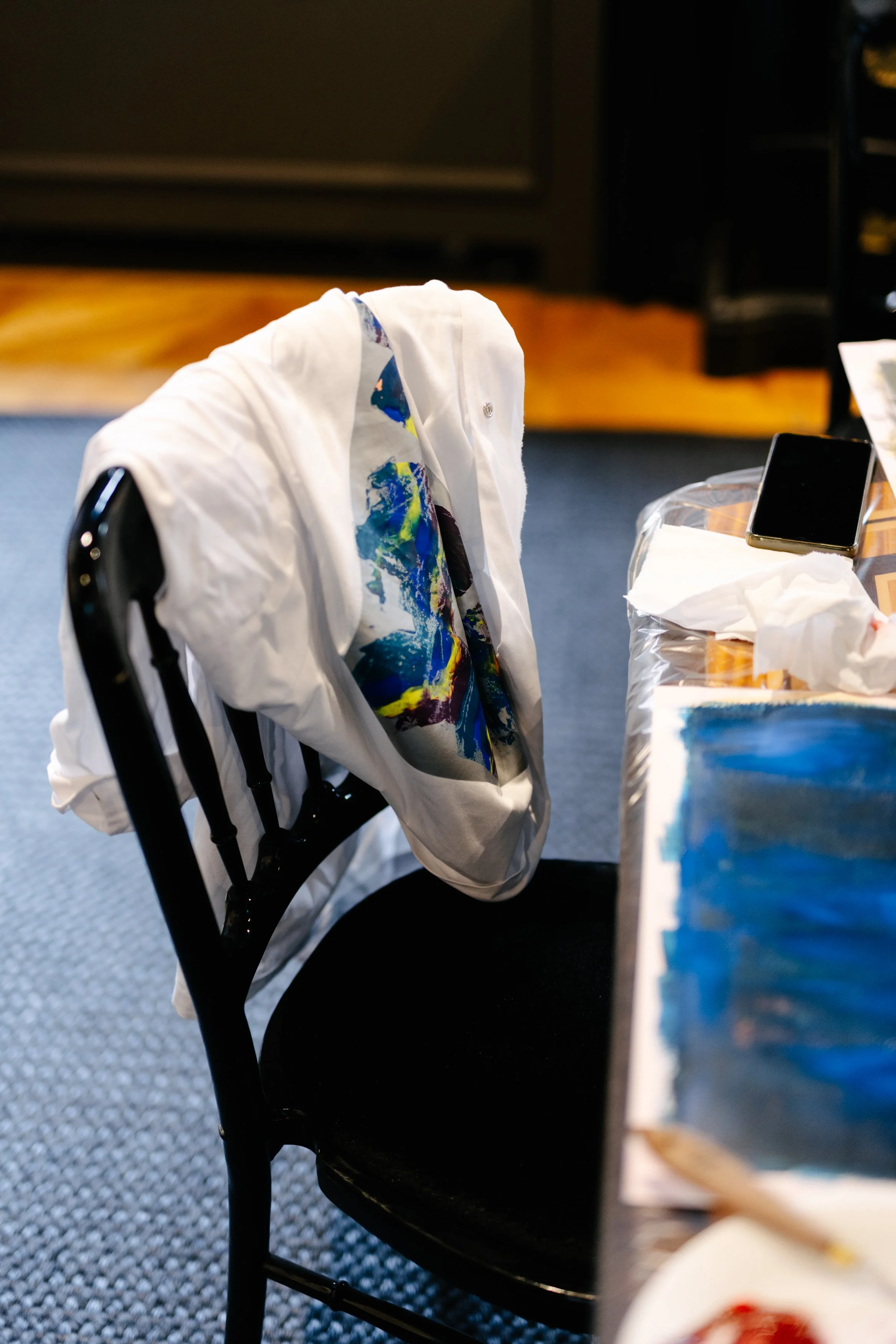 Une chaise avec une veste blanche pendue dessus, à côté d'une table avec des objets, y compris un téléphone portable et un papier.»