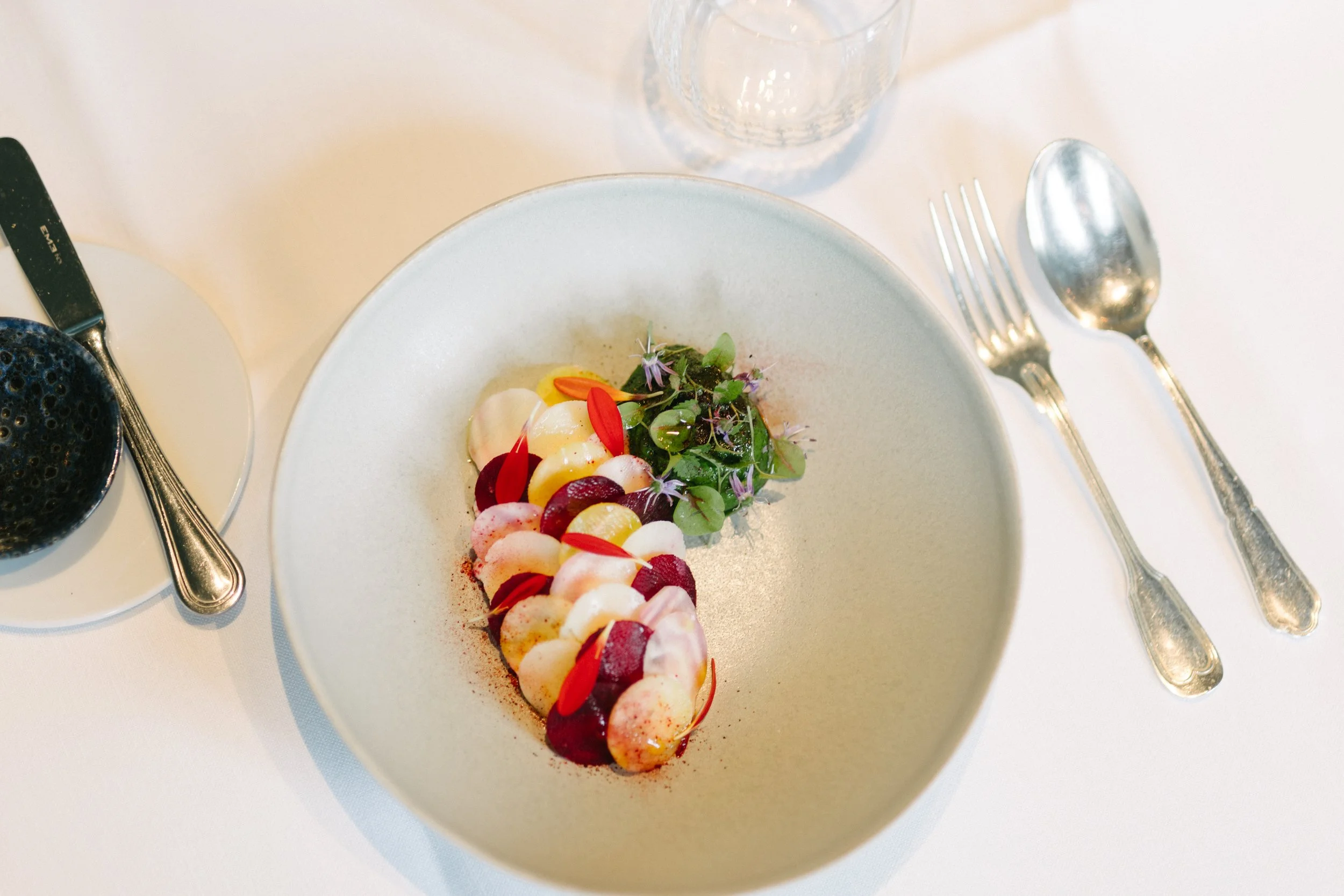 Assiette avec un plat de cuisine moderne, garnie de légumes, fleurs et herbes, vue du dessus