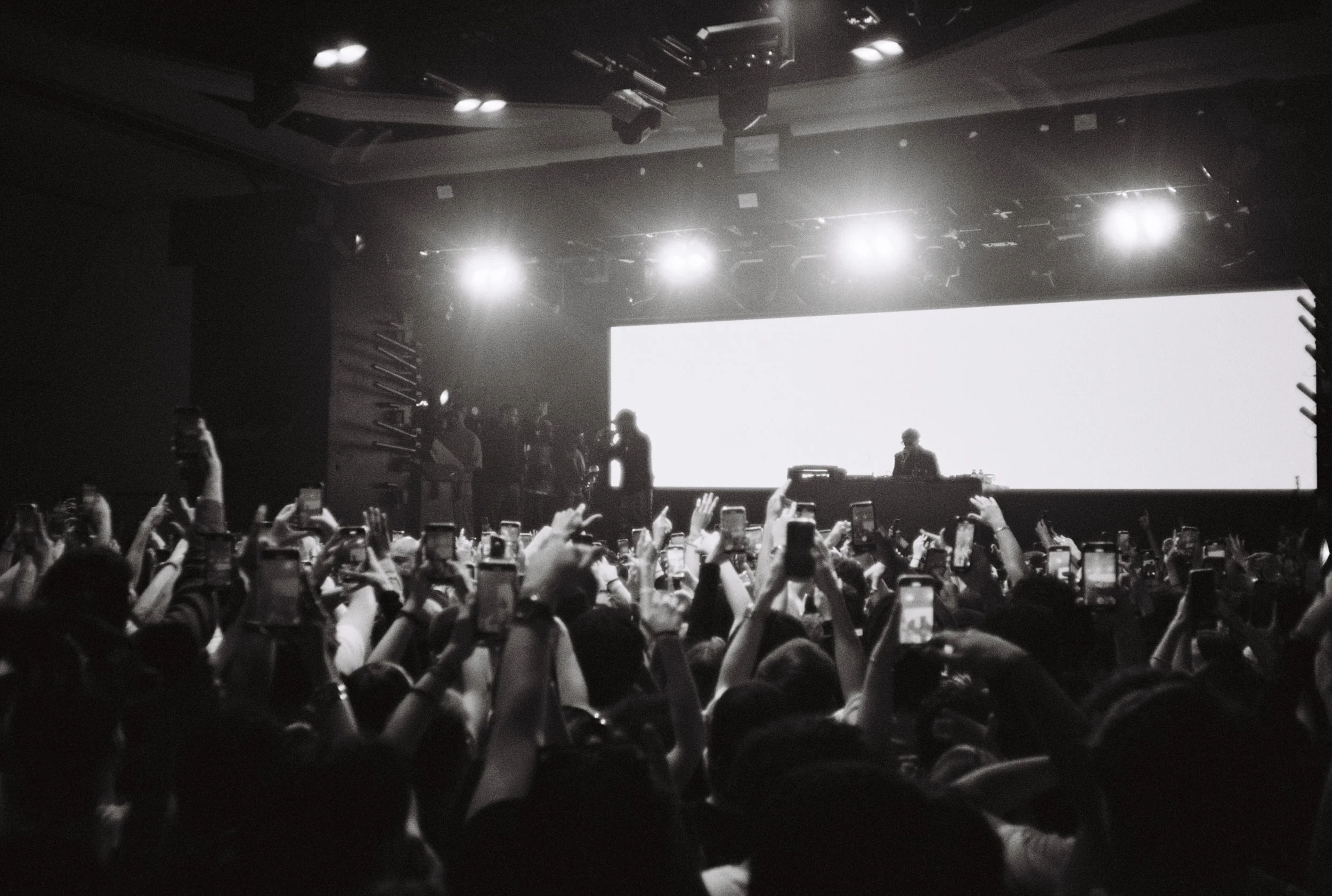 Concert avec un grand écran lumineux, un DJ en arrière-plan et foule nombreuse avec many personnes tenant leurs téléphones en l'air.
