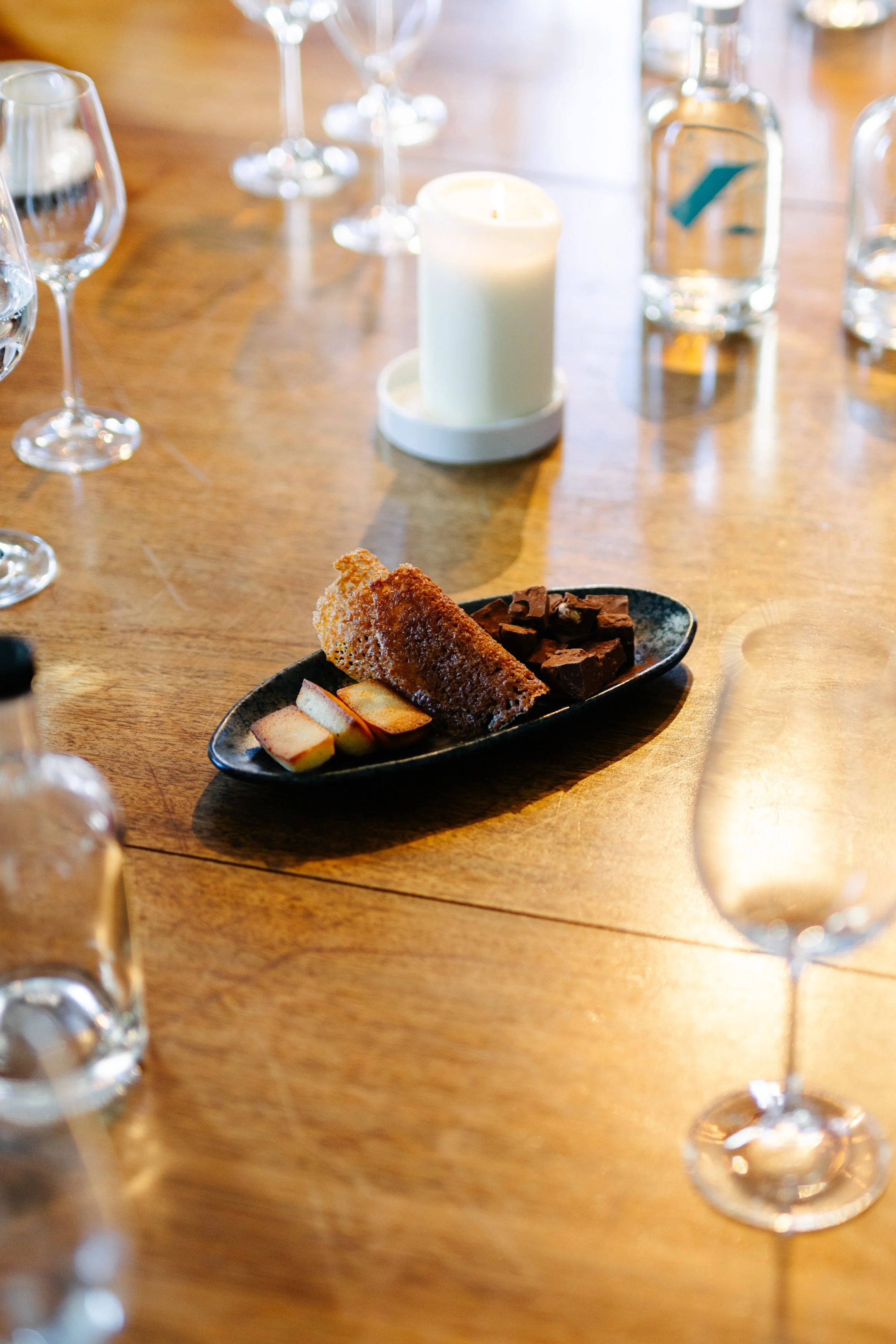 Plate de desserts comprenant un morceau de gâteau, des morceaux de pomme, et des morceaux de chocolat, avec des verres à vin et une bougie sur une table en bois.