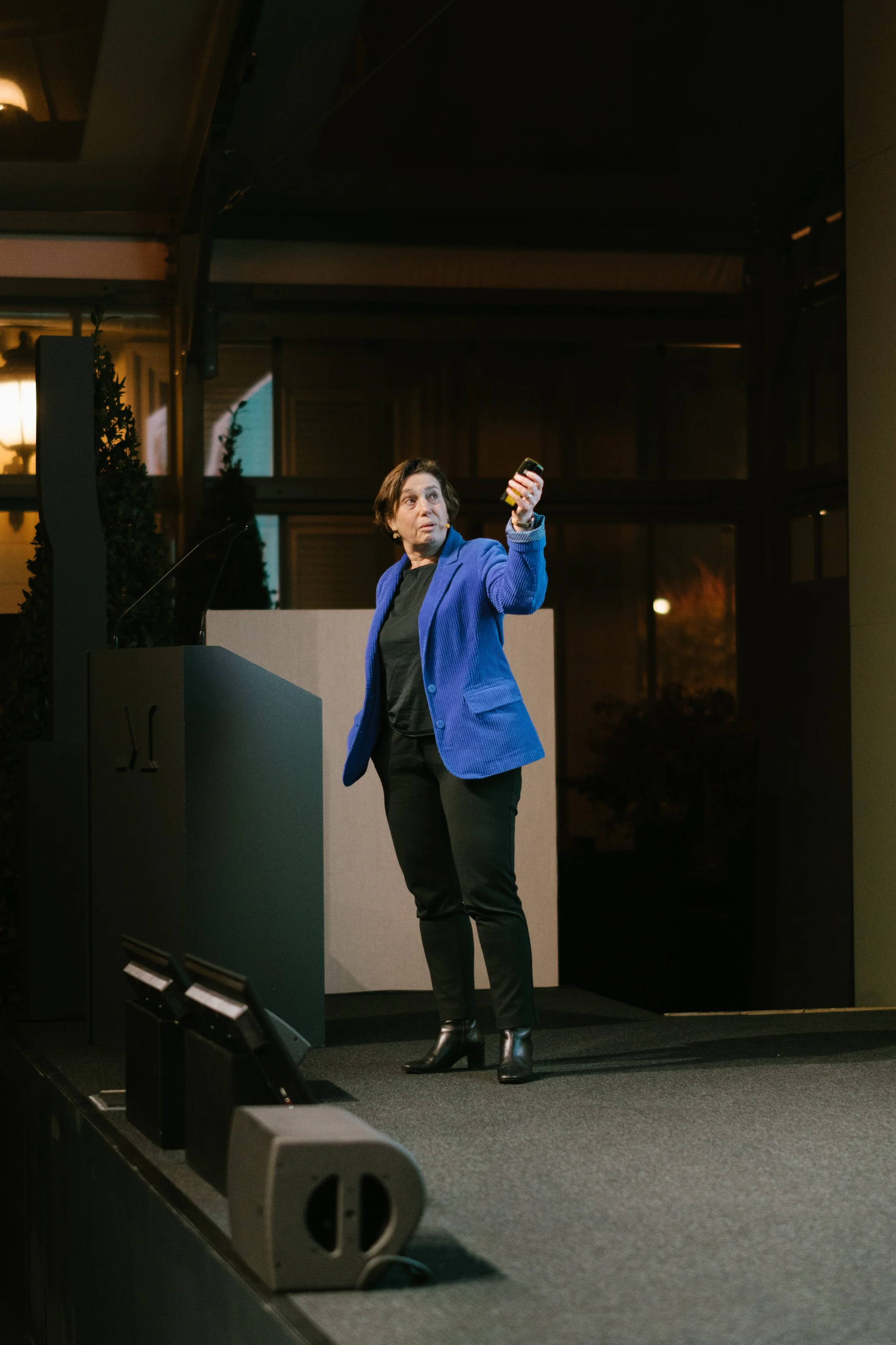 Une femme faisant une présentation sur scène, tenant un téléphone portable, dans un cadre professionnel ou lors d'une conférence.