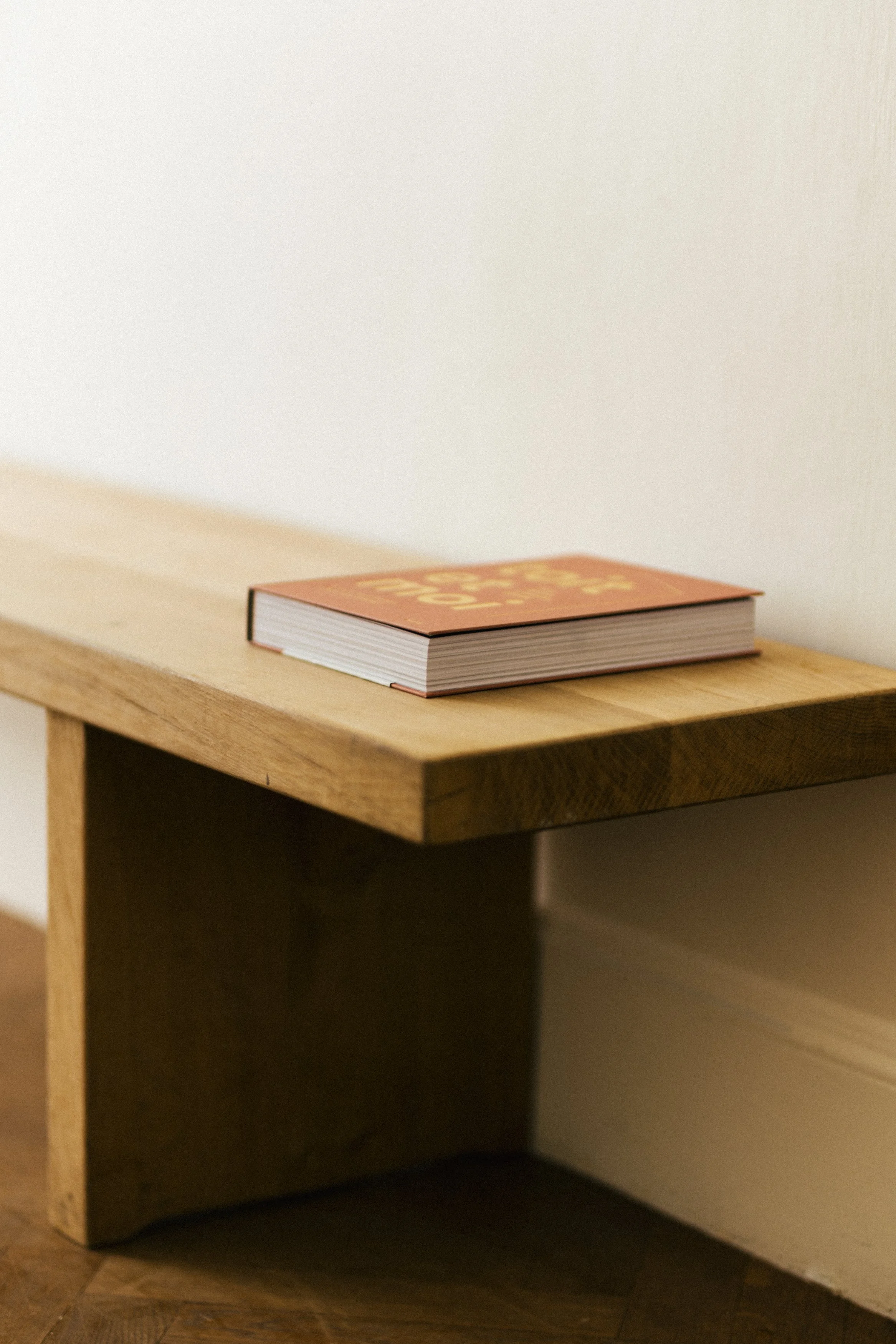 Un livre posé sur une étagère en bois contre un mur blanc.