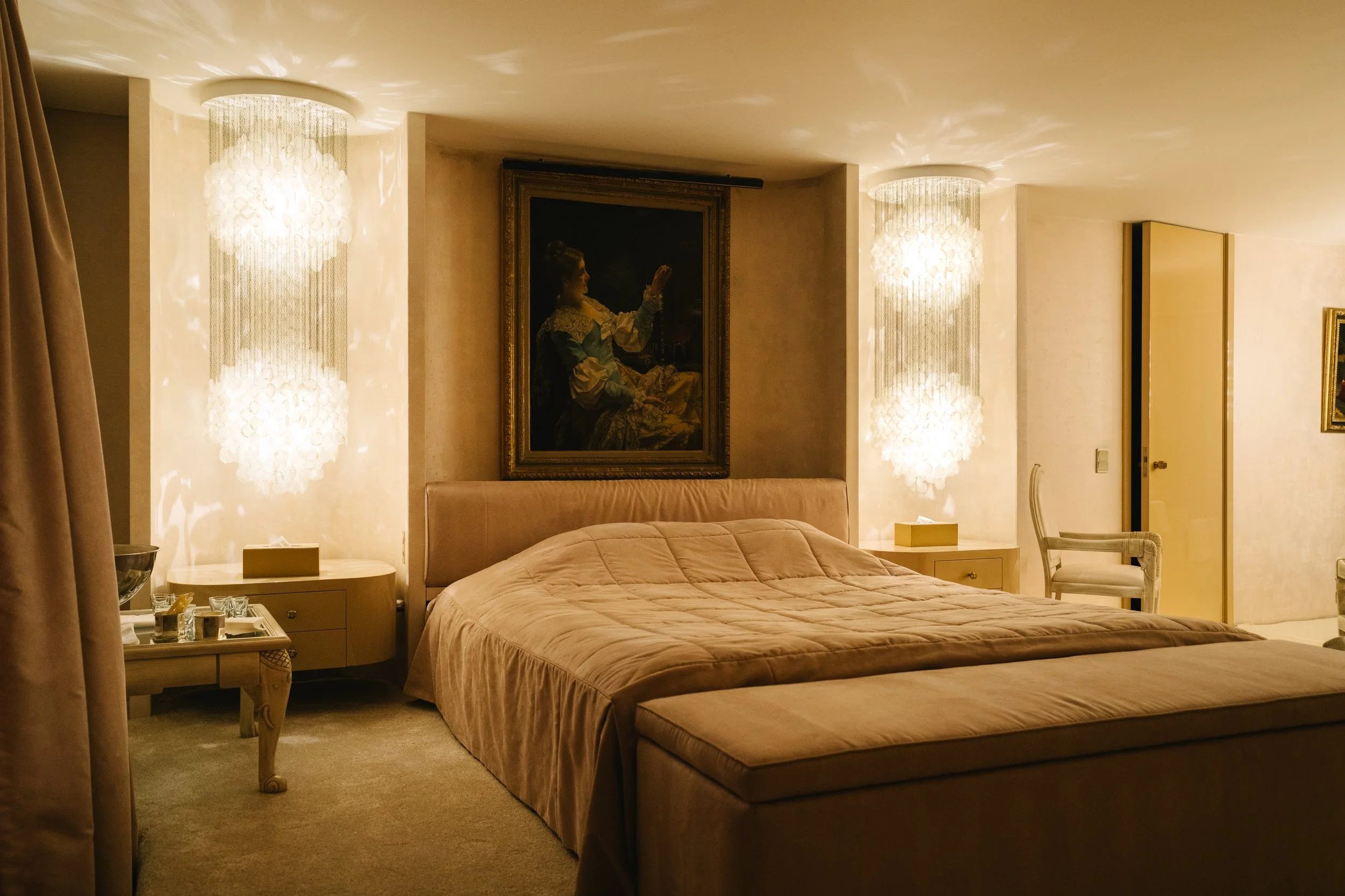 Chambre élégante avec lit, deux lampes décoratives et tableaux aux murs, ambiance chaleureuse.