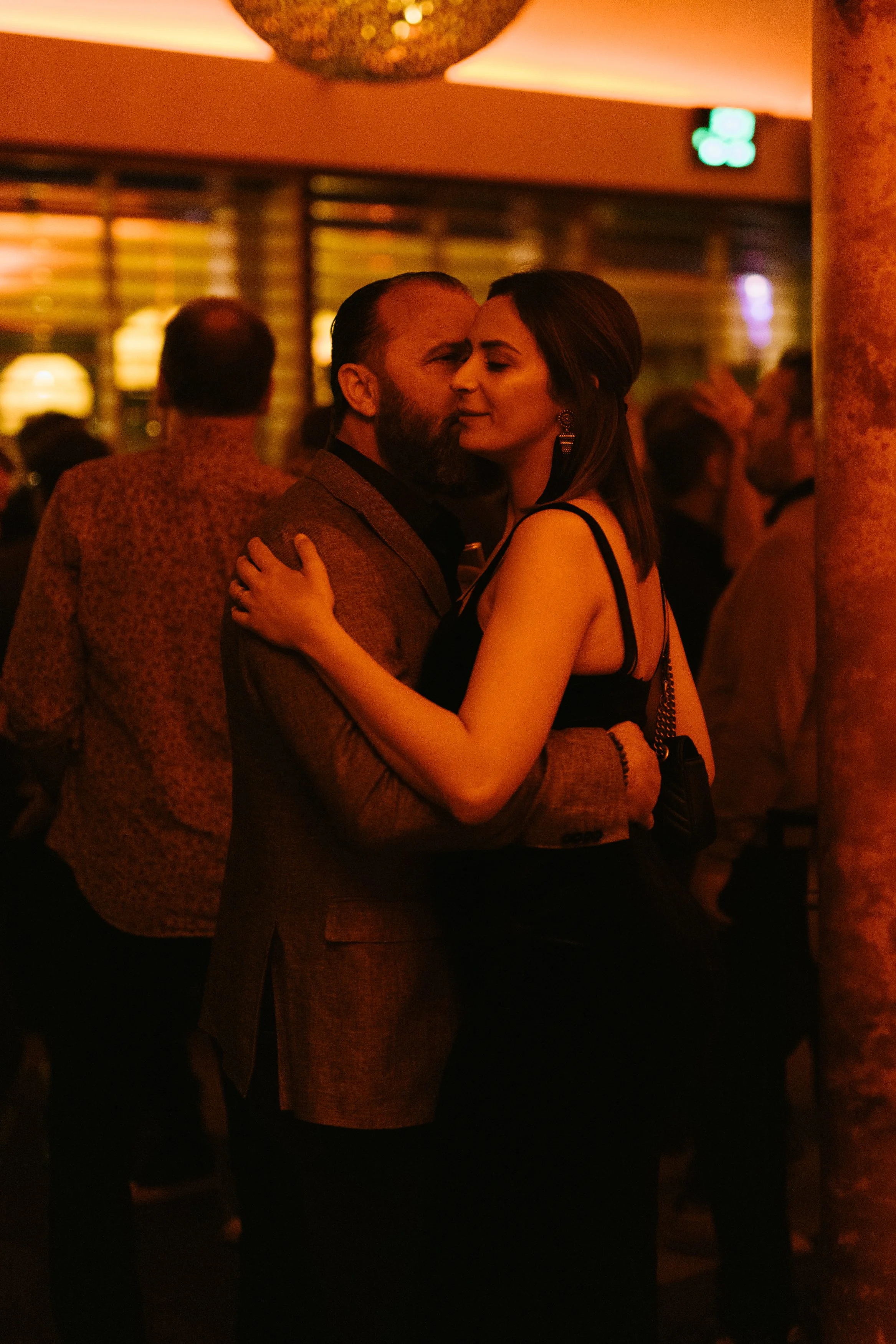 Un couple danse dans une ambiance chaleureuse et intime, avec un éclairage tamisé, lors d'une soirée ou d'événement social.
