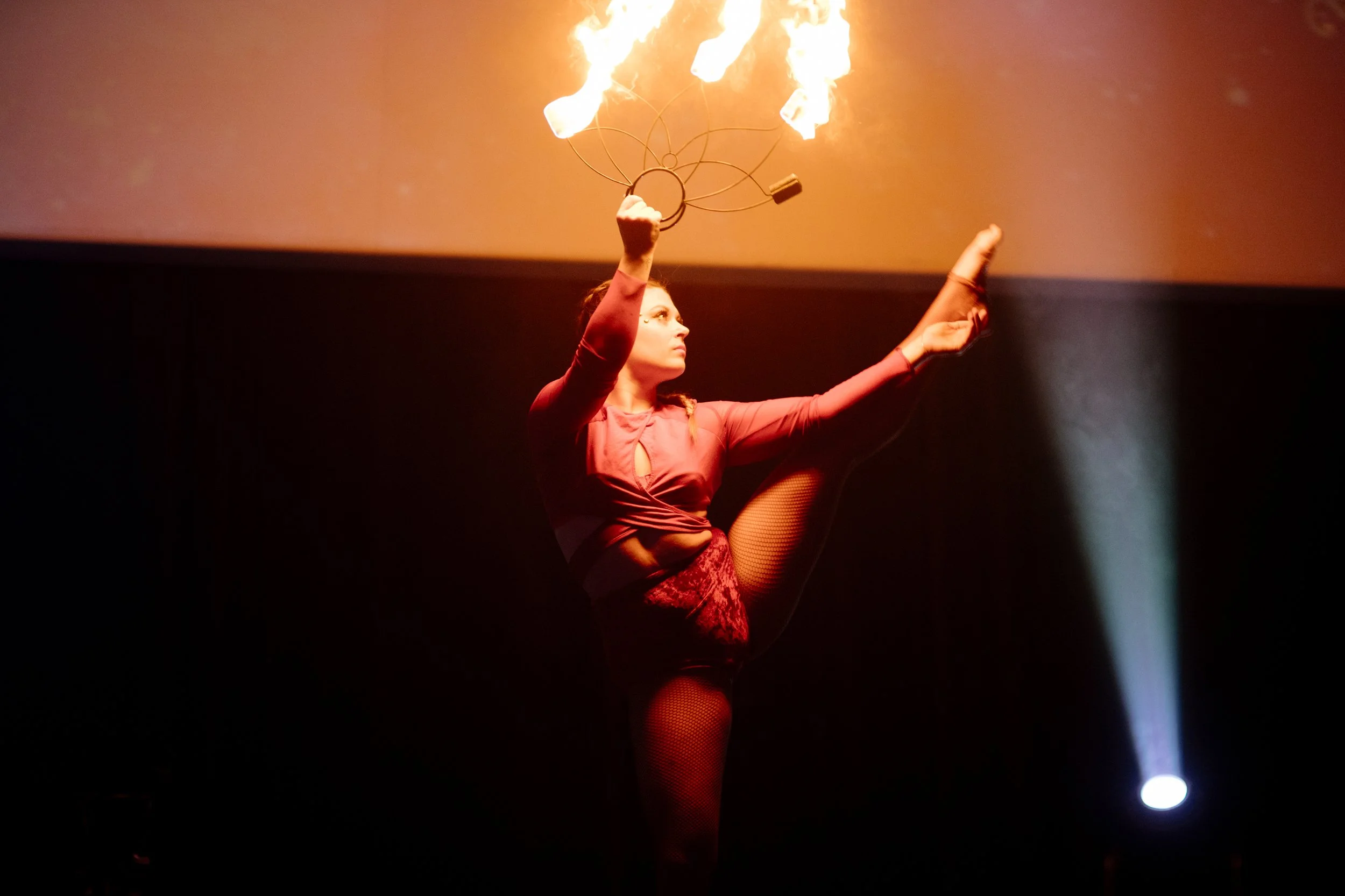 Une femme en costume rouge effects un numéro de jonglerie avec des anneaux en feu sur scène, éclairée par un projecteur.