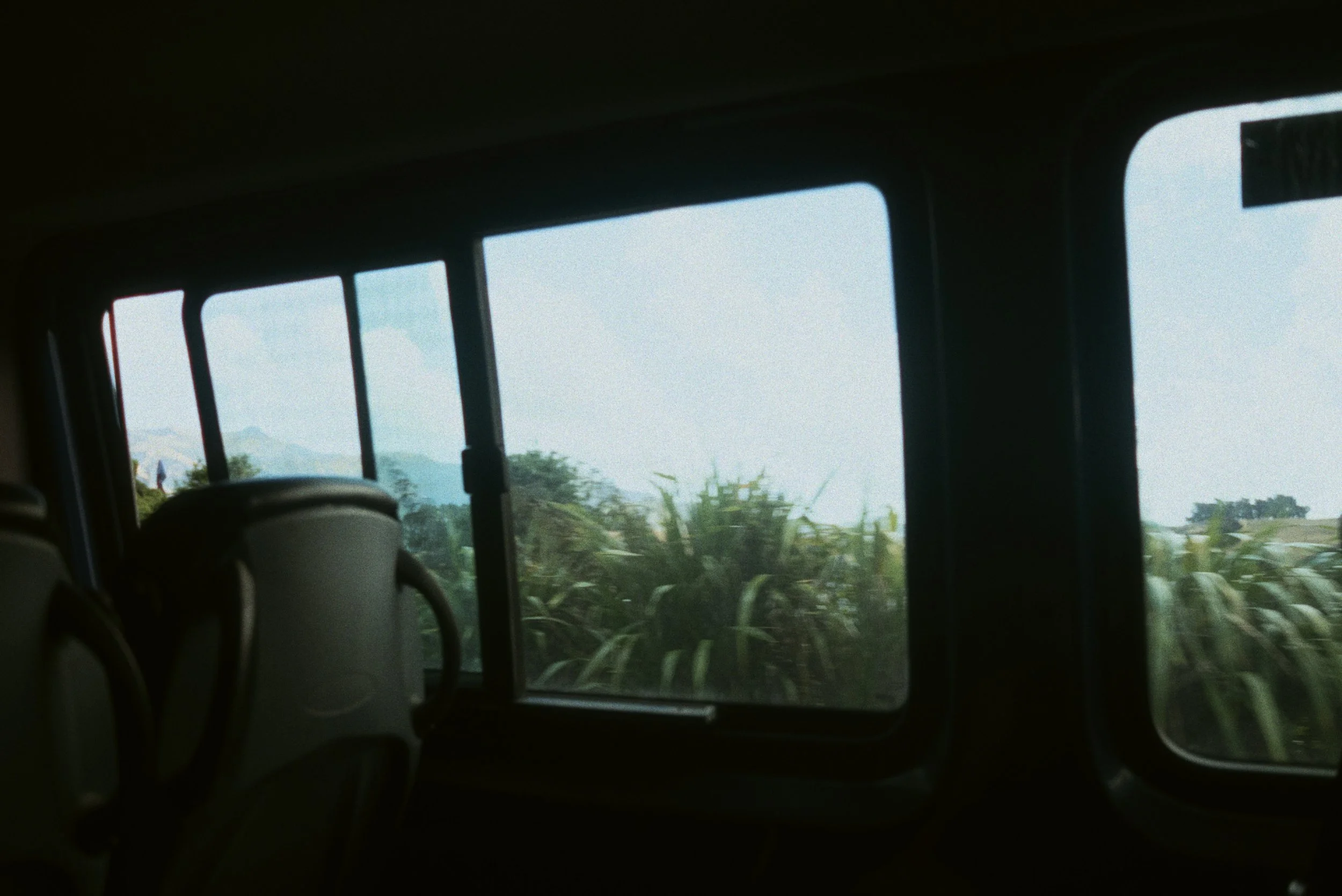 Vue depuis l'intérieur d'un bus avec des sièges, montrant un paysage avec des champs et des montagnes à travers la fenêtre