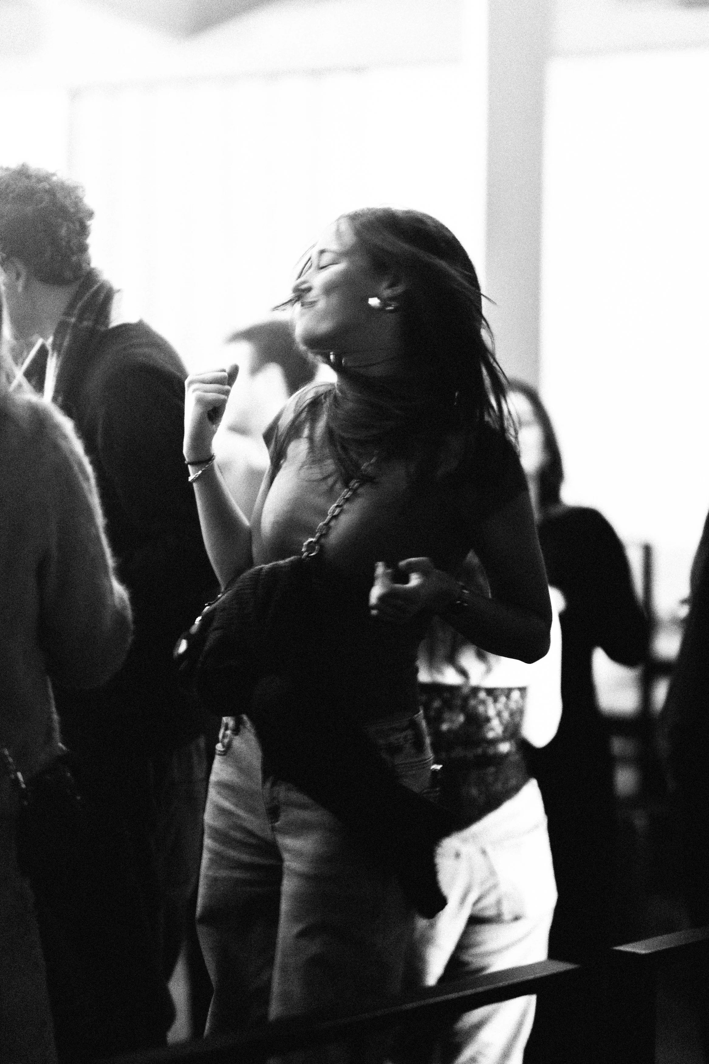 Une femme souriante danse dans une foule, en noir et blanc, avec plusieurs personnes en arrière-plan.