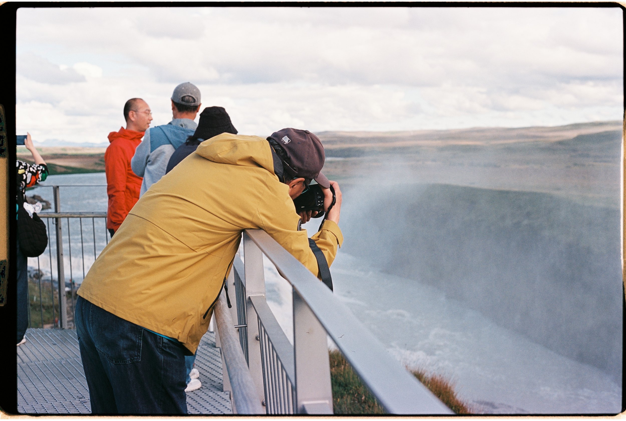 Groupe de personnes observant et prenant des photos d'une chute d'eau spectaculaire dans un paysage naturel.