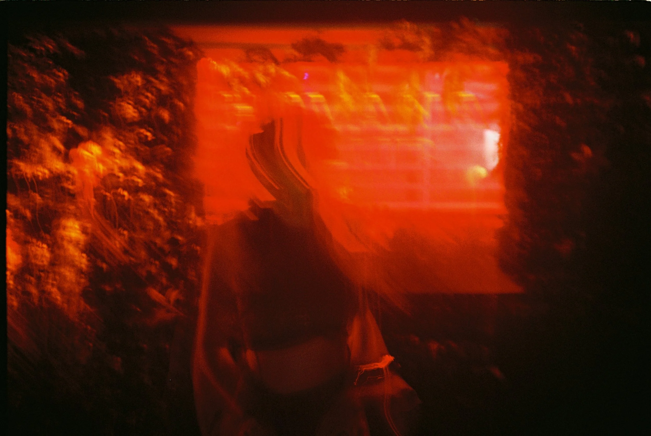 Une personne prend un selfie à l'extérieur, le reflet de la lumière rougeâtre et le flou créent une atmosphère mystérieuse.