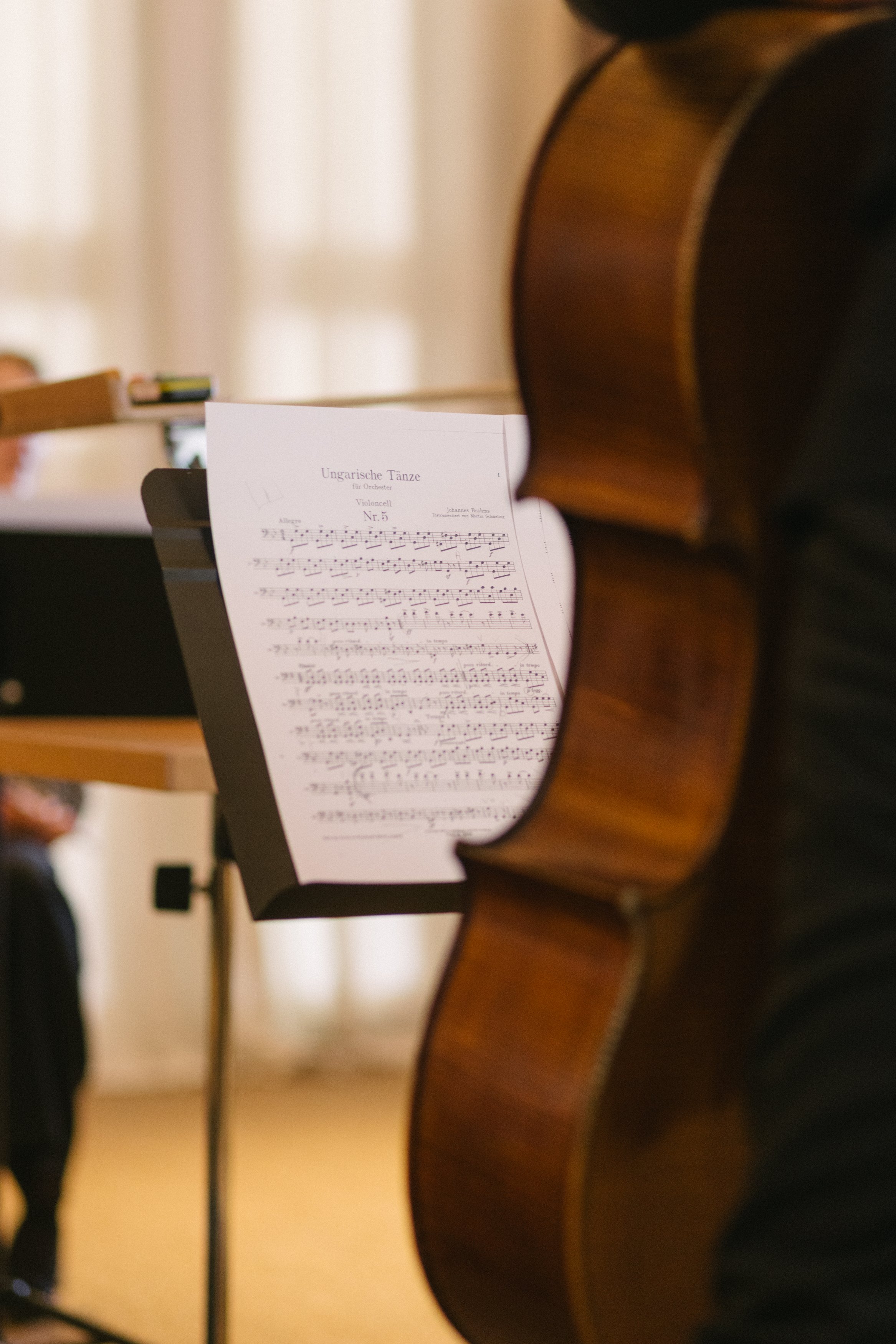 Une partition musicale intitulée 'Ungarische Tänze' pour violoncelle est placée sur un support à côté d'un violoncelle dans une salle de musique ou de répétition.