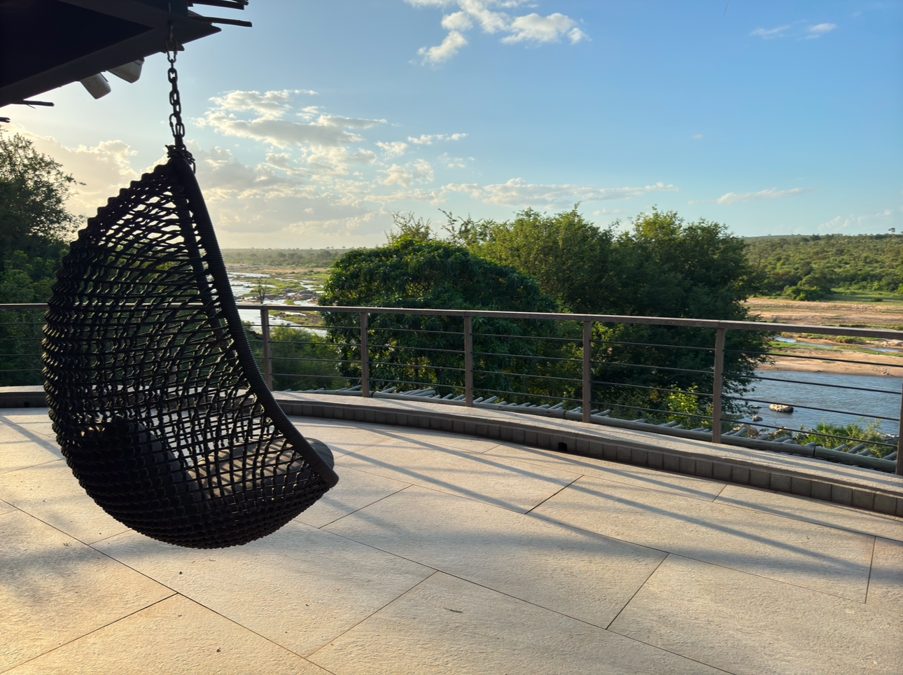 View from the lodge deck overlooking the Crocodile River and Kruger National Park, with a hanging chair and river landscape in the distance.