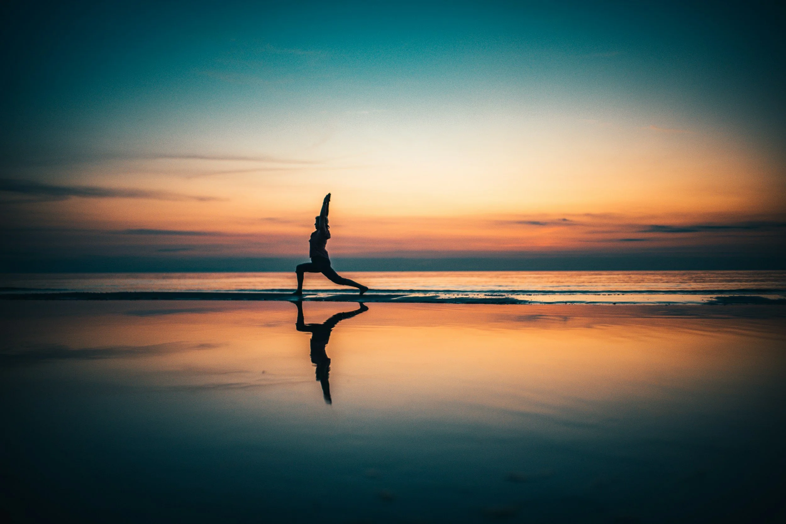 Person practicing yoga on the beach during sunset with their reflection in the wet sand.