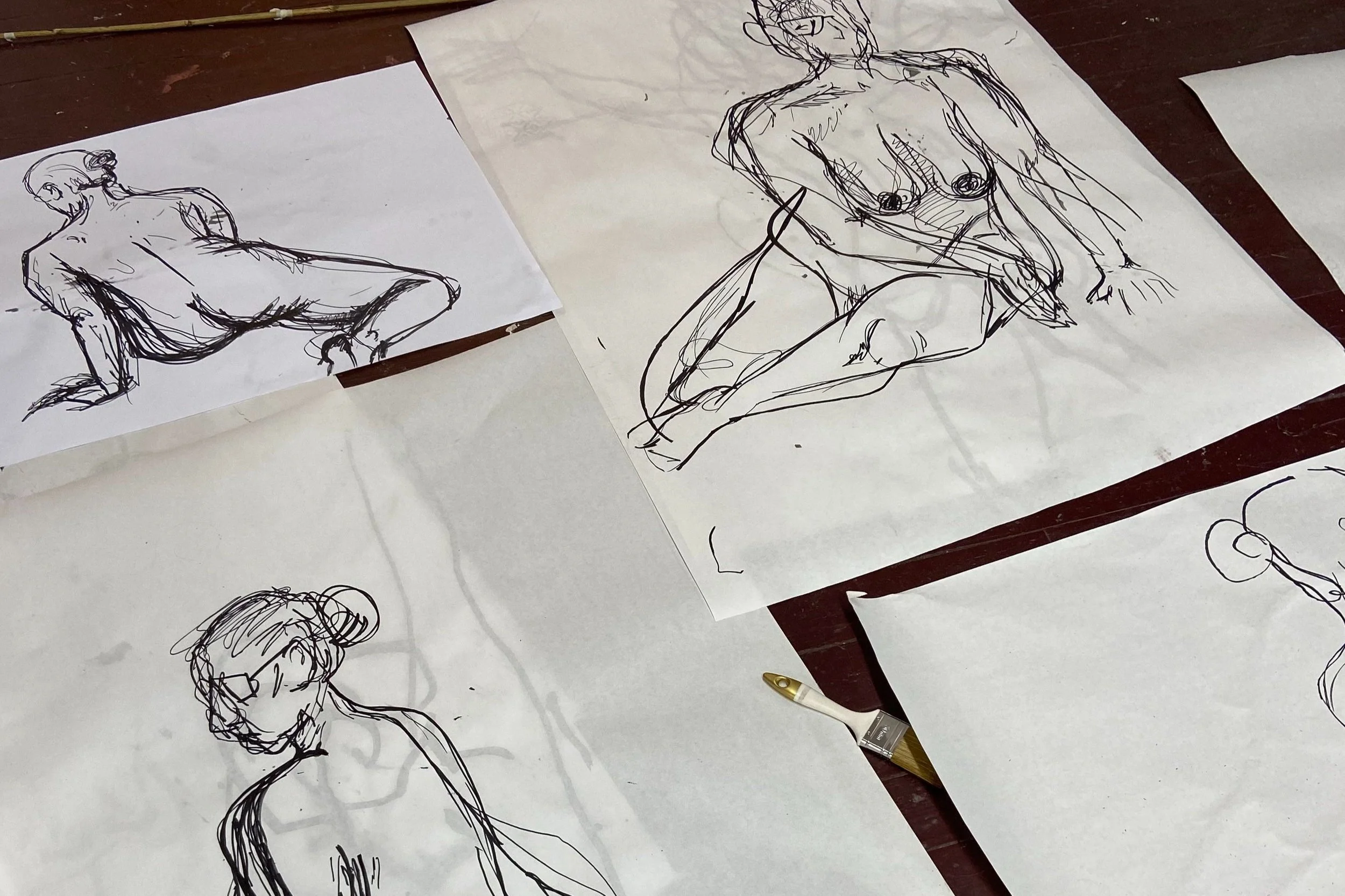 Skisser av menneskekropper i ulike positurer tegnet med penn på hvitt papir, lagt ut på et bord.