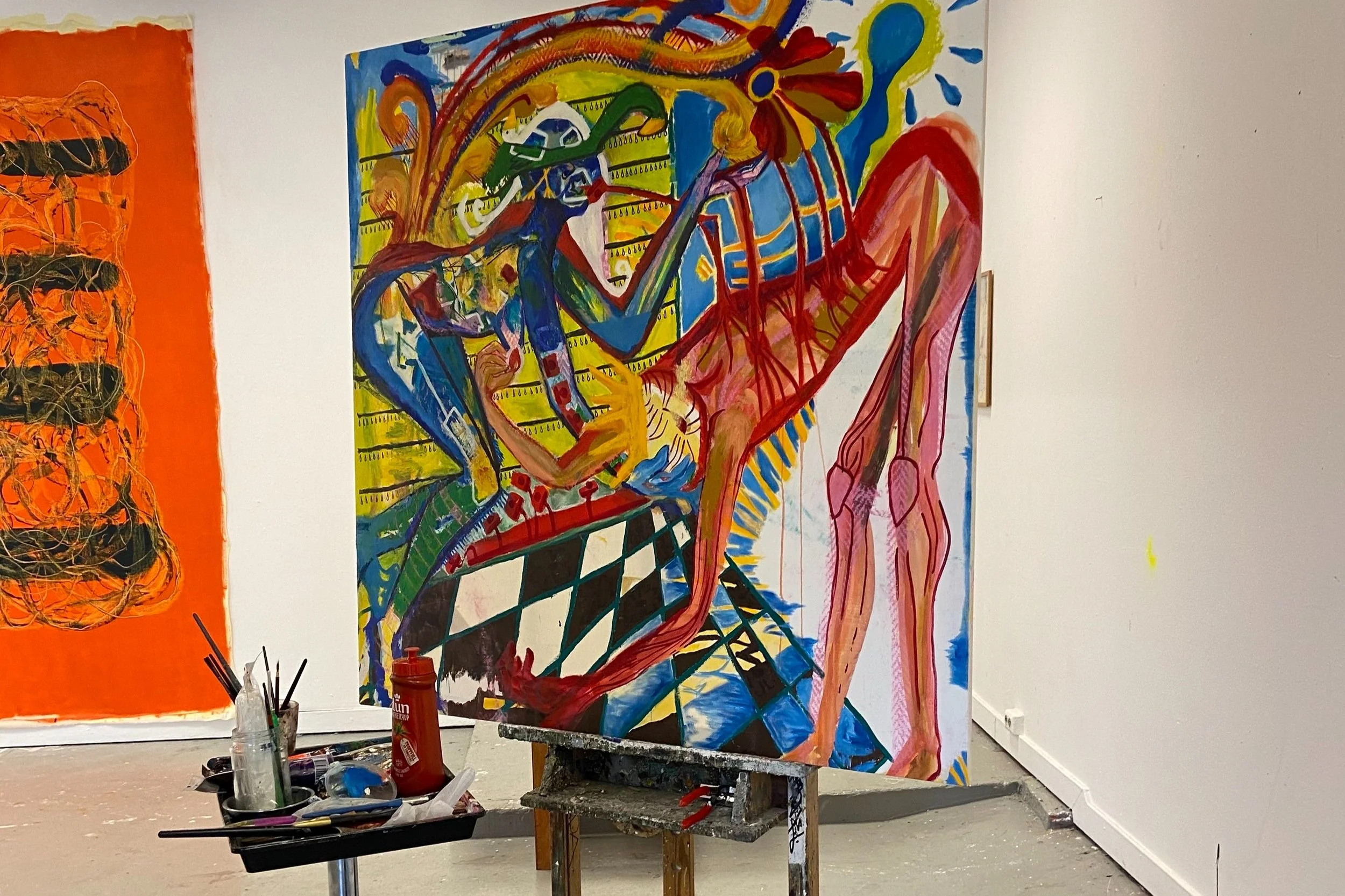 Et fargerikt abstrakt maleri på et lerret, plassert på et staffeli. Maleriet viser en surrealistisk scene med geometriske former, mennesker og sterke farger som blå, rød og gul, i en kunstnerisk, ekspressiv stil.